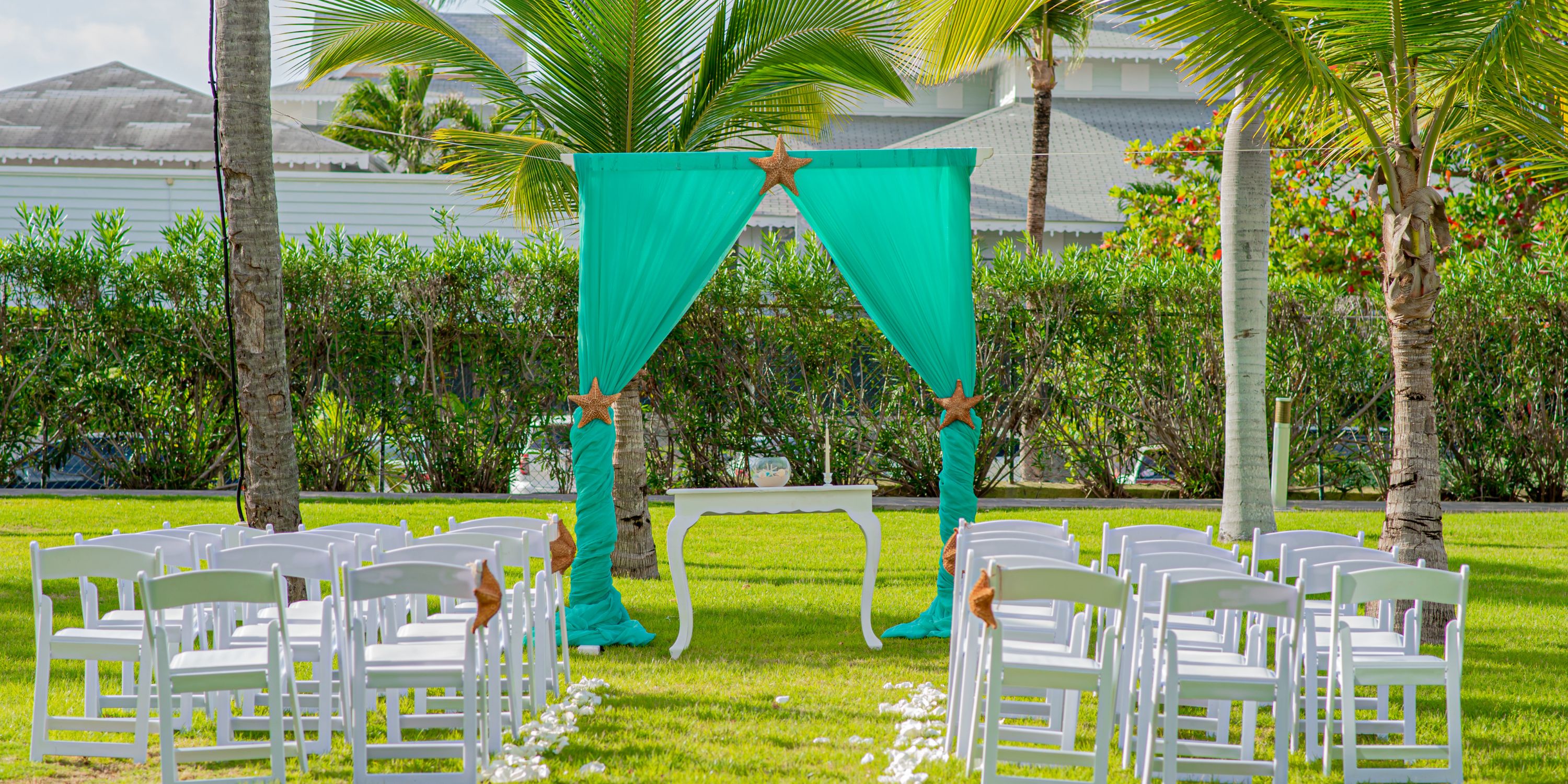 Destination wedding setup at Hotel Riu Palace Punta Cana with white chairs, turquoise drapes, and palm trees.