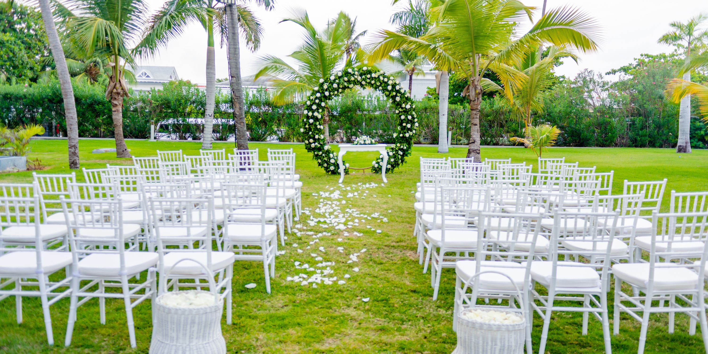 Destination wedding ceremony at Hotel Riu Palace Punta Cana with white chairs and a floral arch on the lawn.
