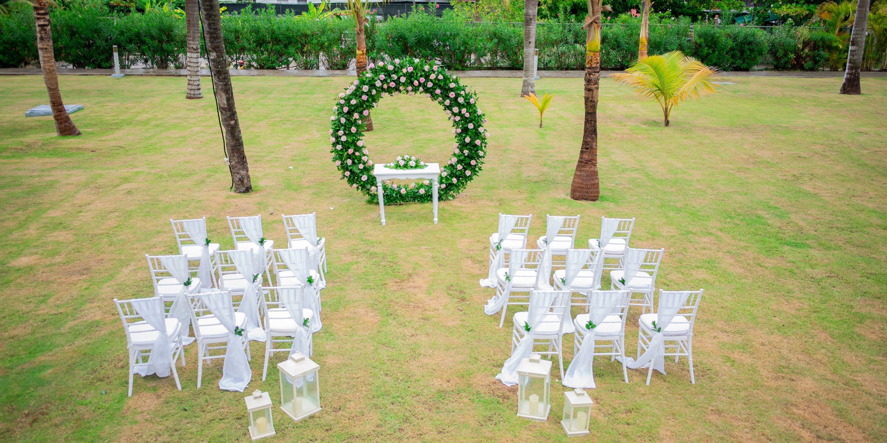 Destination wedding ceremony at Hotel Riu Palace Punta Cana with white chairs, lanterns, and floral arch.