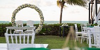 Destination wedding scene with white chairs, a table, and floral arch on the beach at Hotel Riu Palace Peninsula.