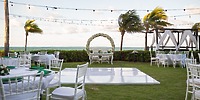 Destination wedding setup by the ocean at Hotel Riu Palace Peninsula with white chairs, floral arch, and lights.