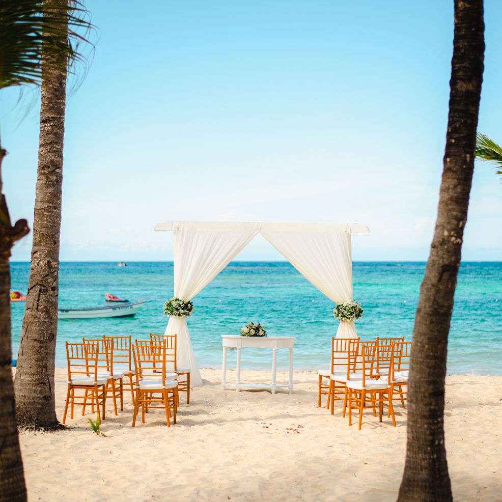 Destination wedding scene featuring white drapes, wooden chairs, and the ocean as a stunning backdrop.
