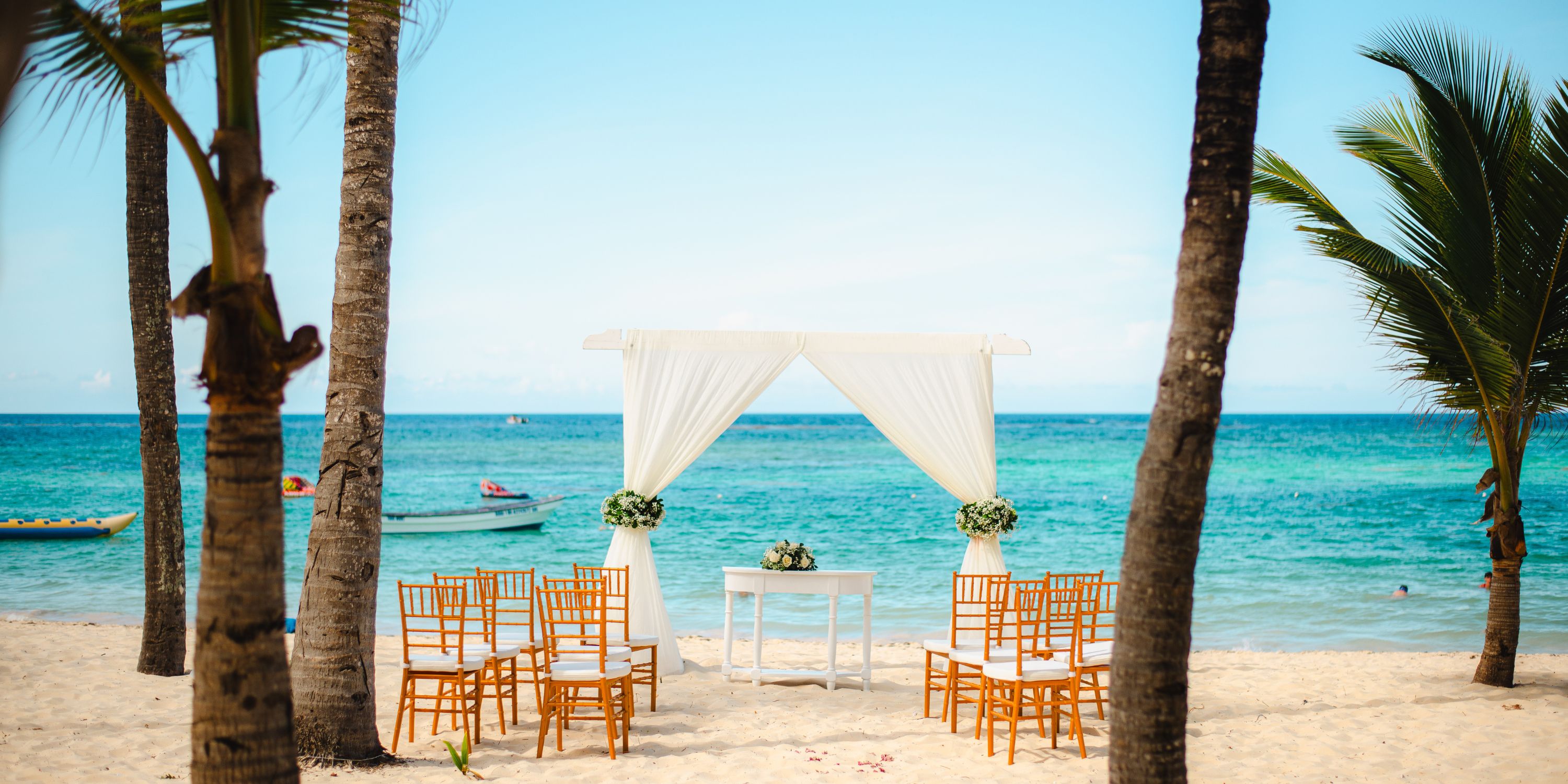 Destination wedding setup on the beach with white chairs, a table, and a canopy by the ocean.