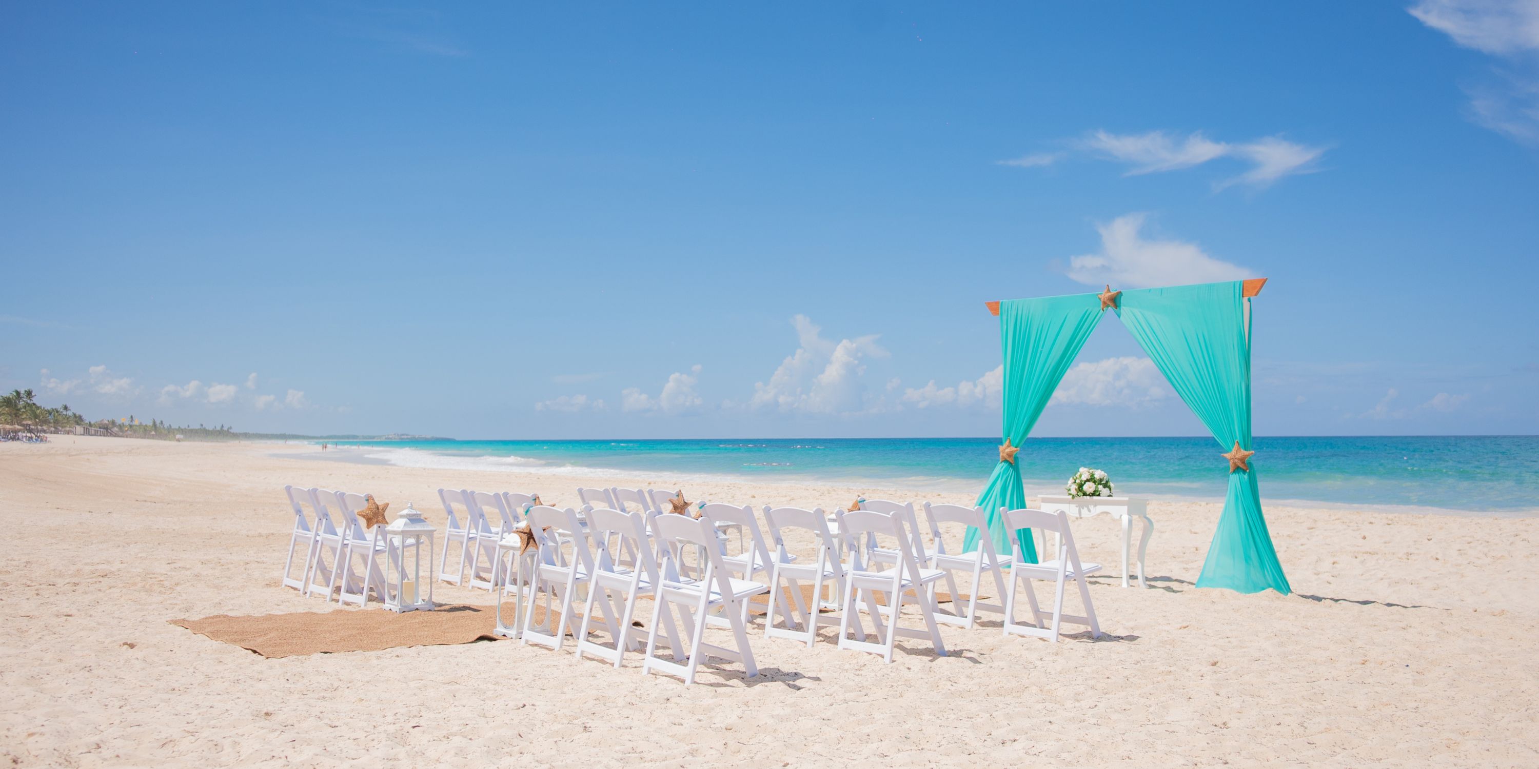 White chairs and a turquoise arch set up for a destination wedding on the sandy beach at Hotel Riu Republica.