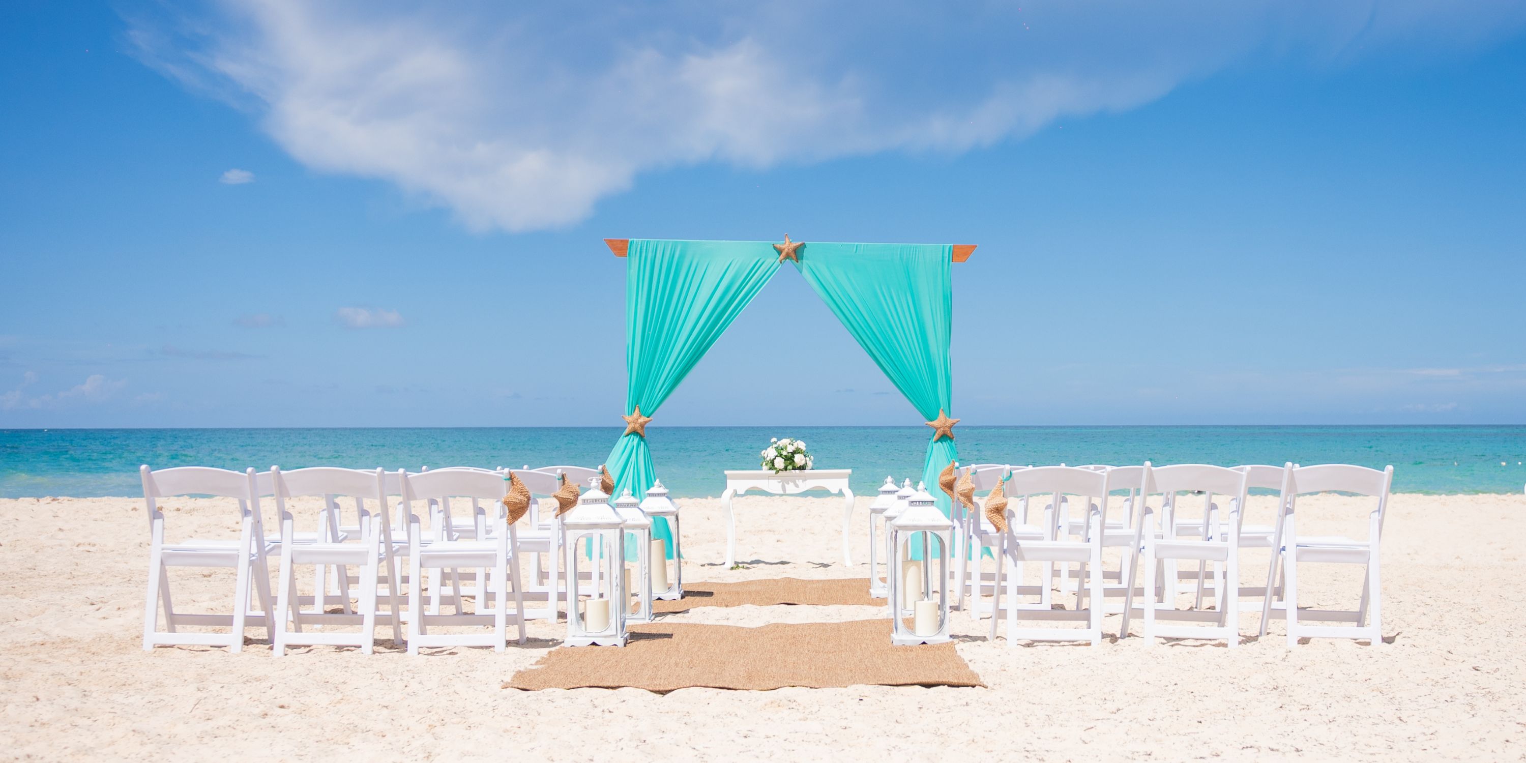 White chairs and a turquoise arch set up for a destination wedding on the sandy beach at Hotel Riu Republica.