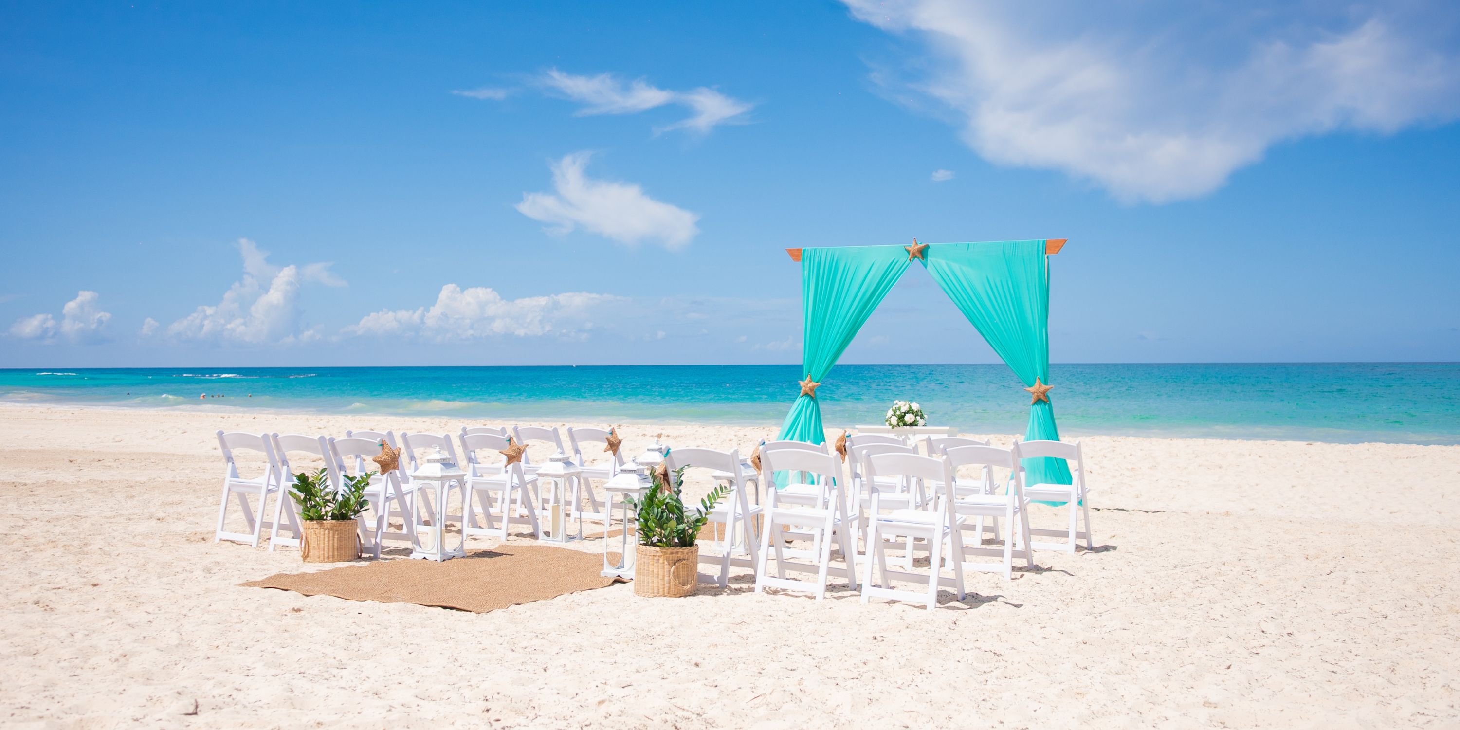 White chairs and a teal arch arranged for a destination wedding on the sunny beach at Hotel Riu Republica.