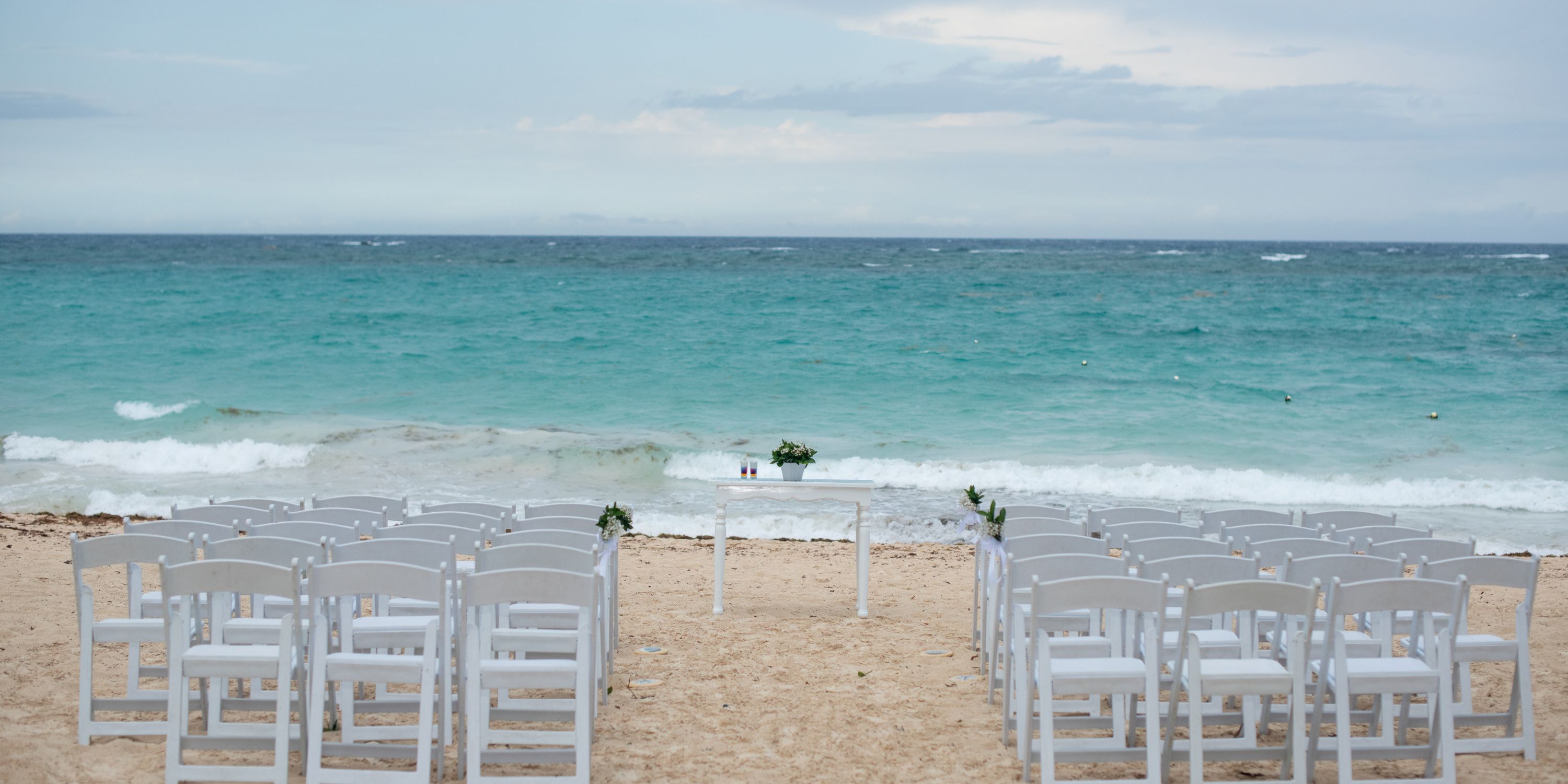 White chairs set up for a destination wedding ceremony at Hotel Riu Republica, overlooking the ocean.