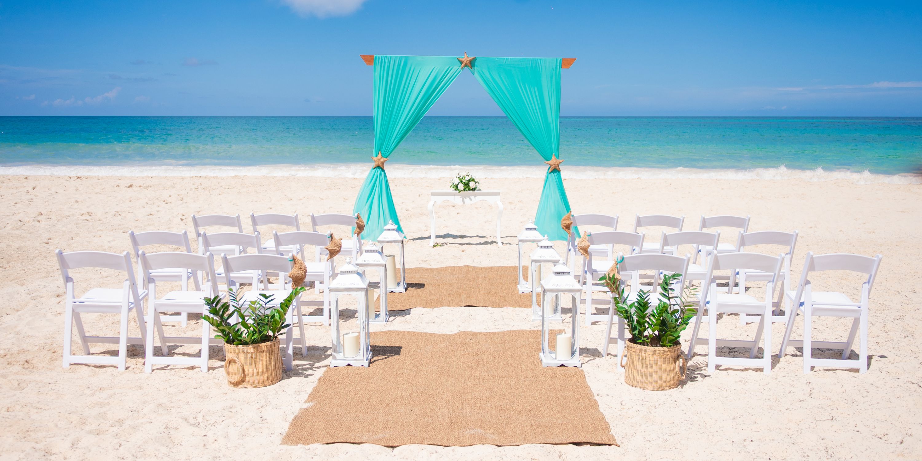 Destination wedding setup at Hotel Riu Republica with white chairs, turquoise arch, and tropical plants.