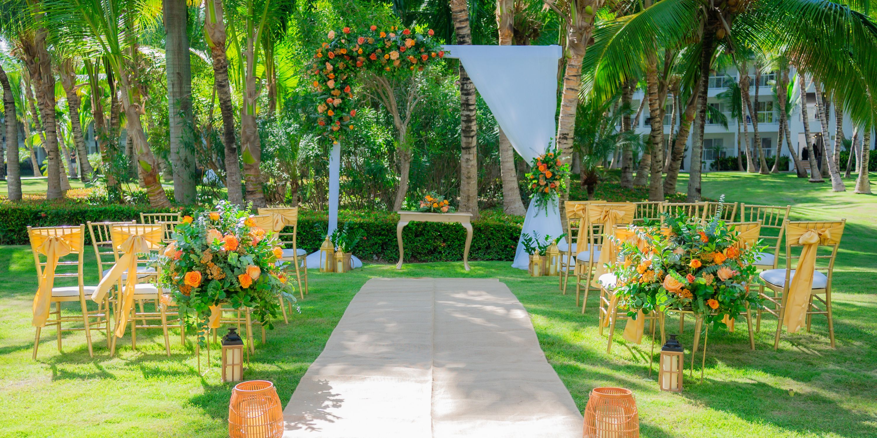 Destination wedding ceremony at Hotel Riu Republica with yellow chairs, orange flowers, and lush greenery.