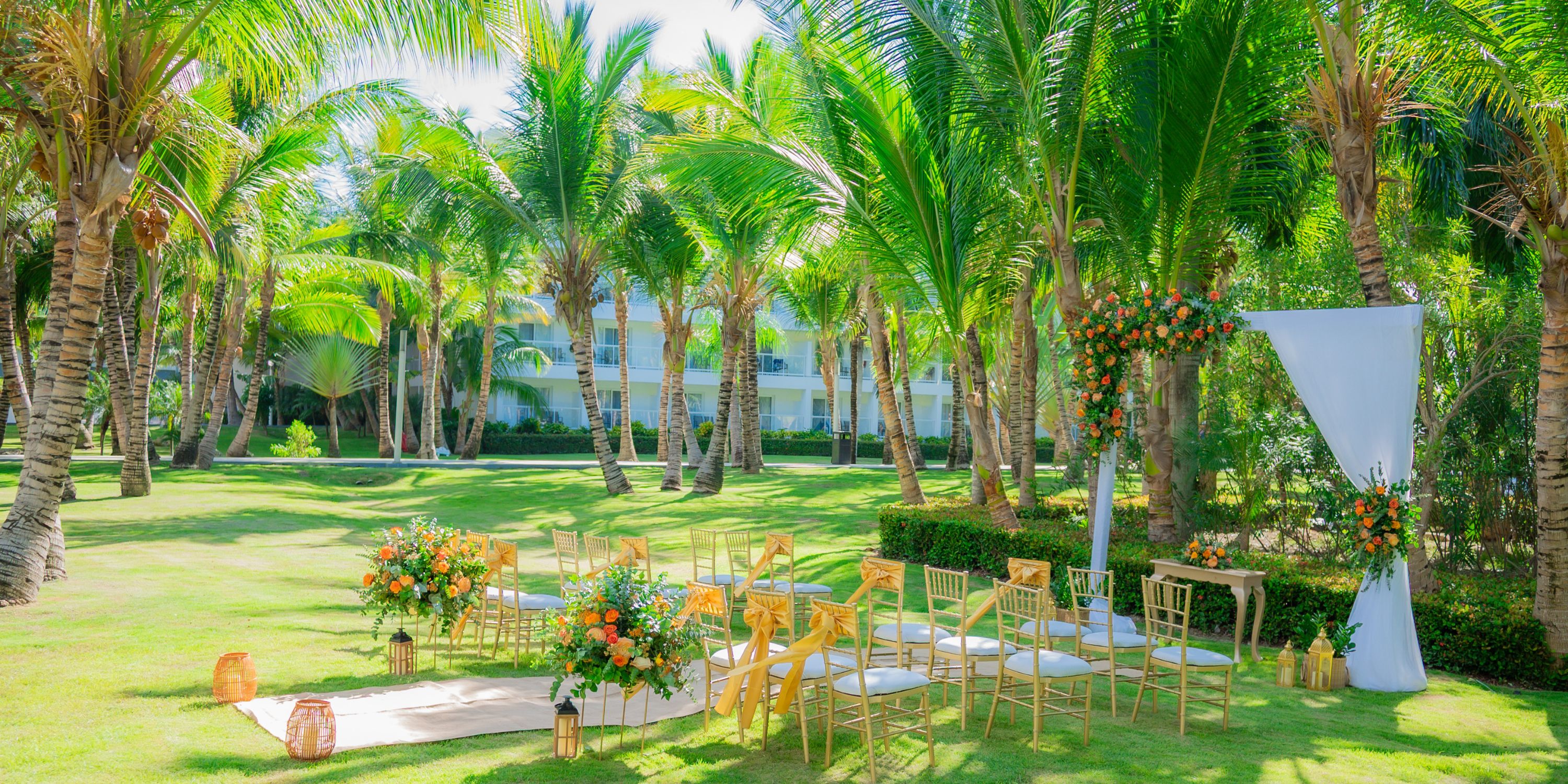 Destination wedding ceremony at Hotel Riu Republica, chairs and flowers arranged beneath palm trees.