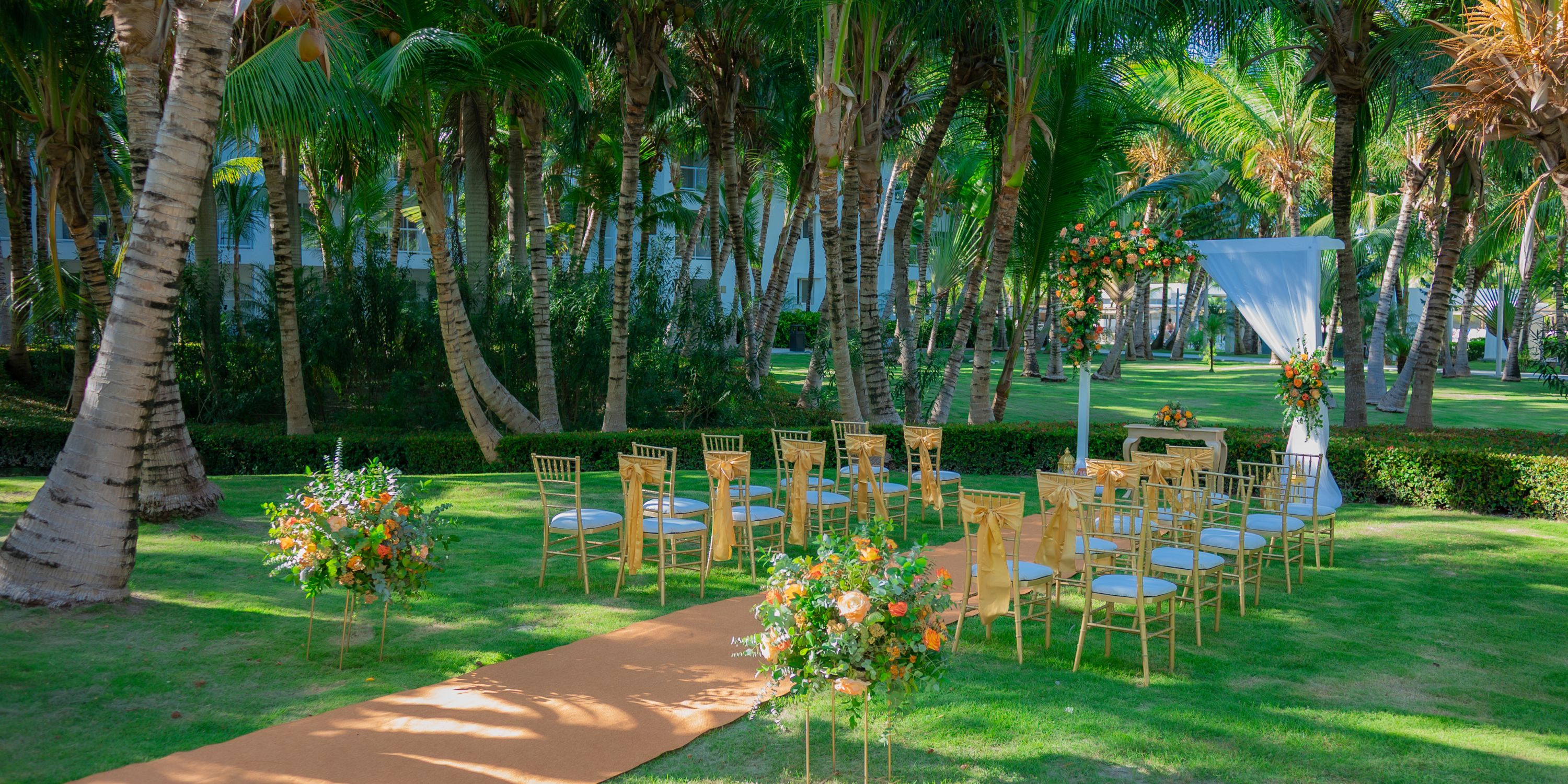 Destination wedding at Hotel Riu Republica with gold chairs and floral decorations set beneath palm trees.