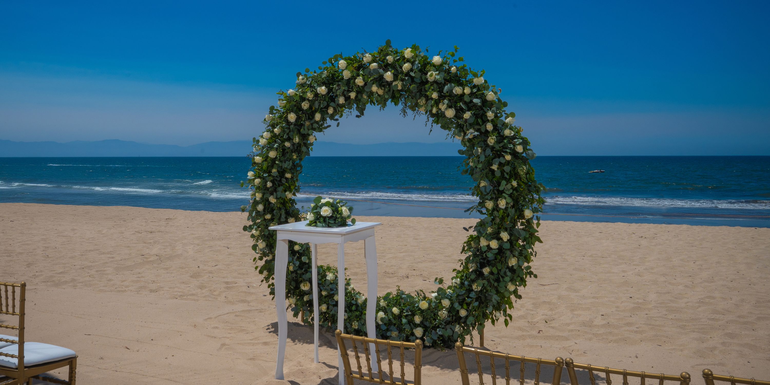 Destination wedding arch and table set up on the beach at Hotel Riu Vallarta overlooking the ocean.
