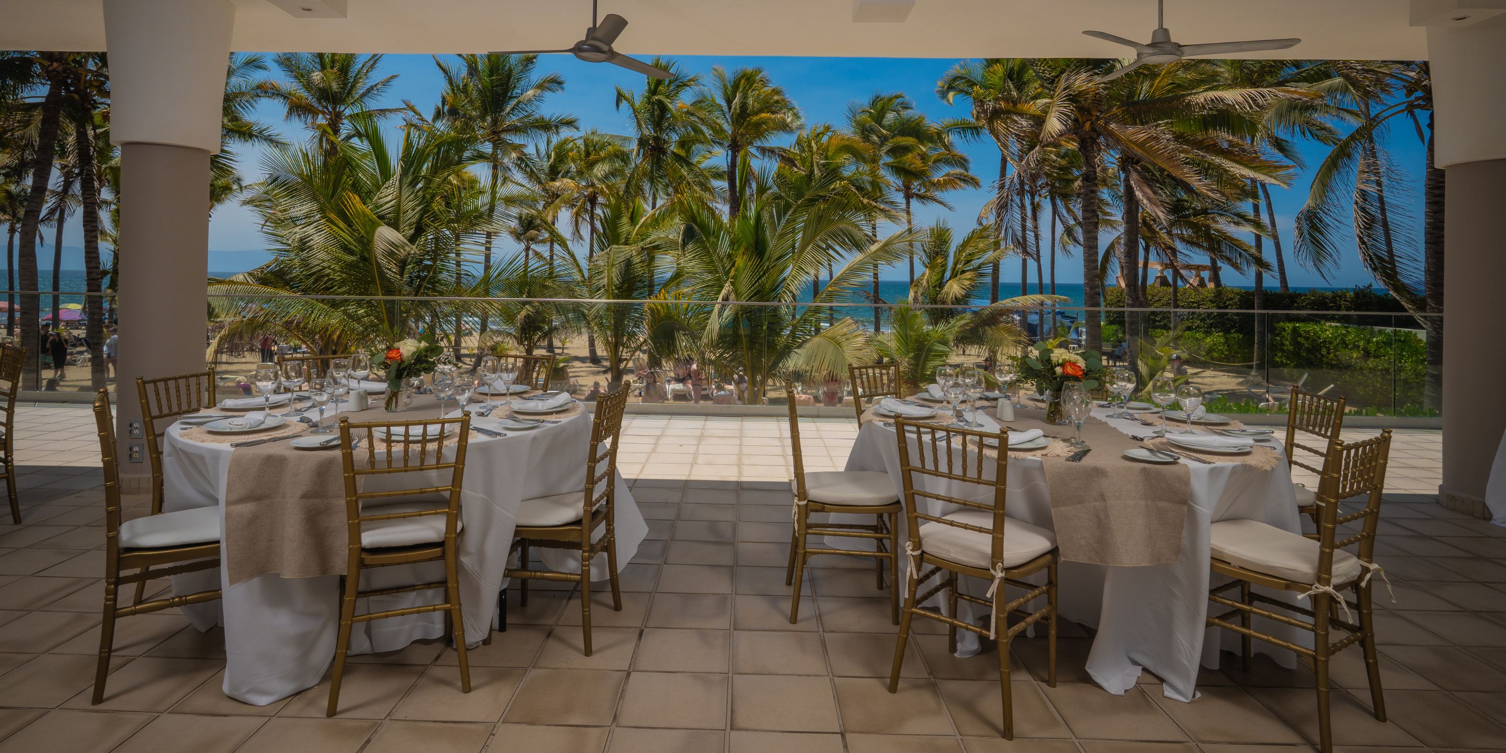 Wedding tables arranged on a covered patio at Hotel Riu Vallarta, with ocean and palm tree views.