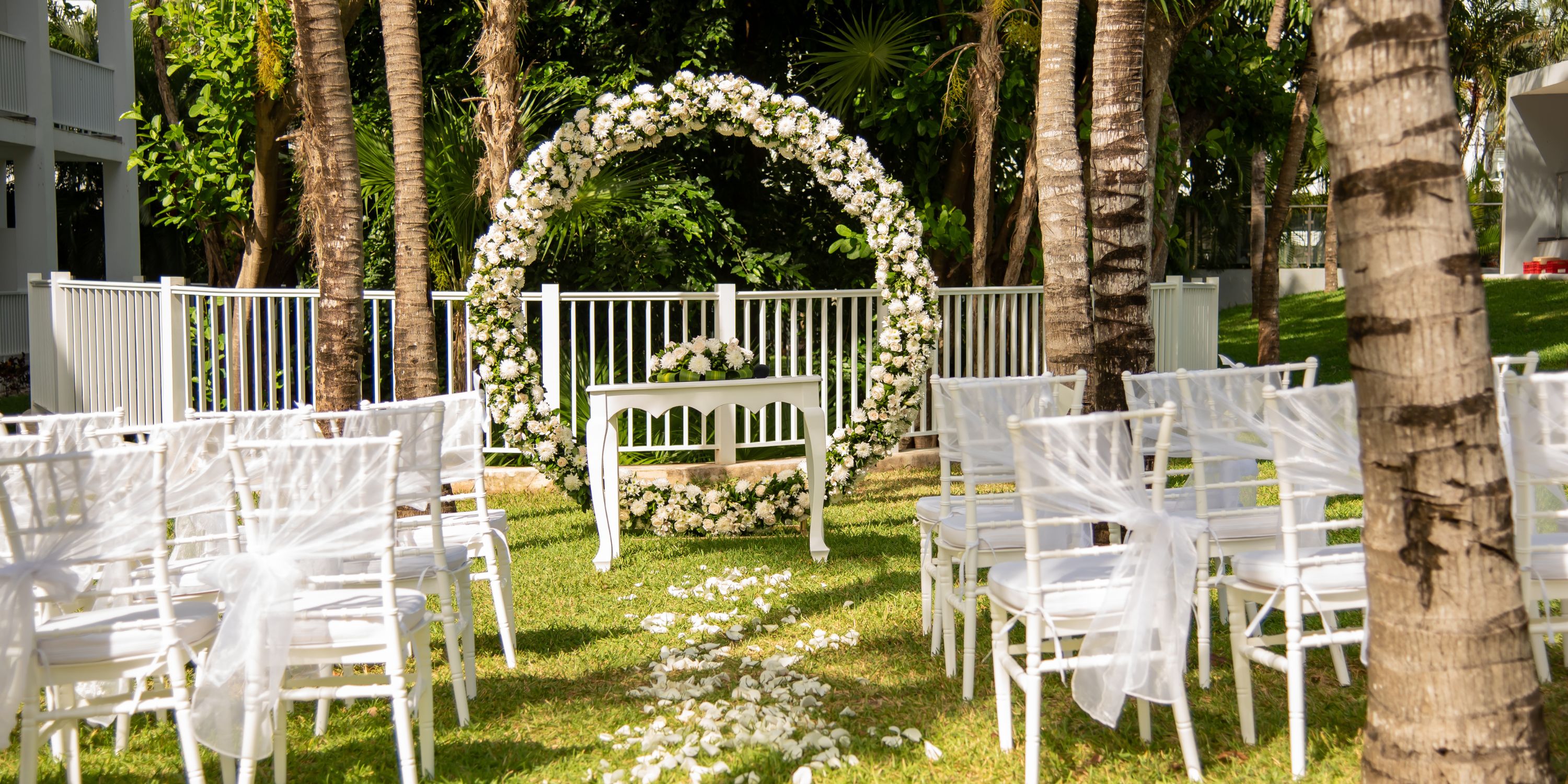 Destination wedding setup at Hotel Riu Yucatan with white chairs, a floral arch, and scattered petals.
