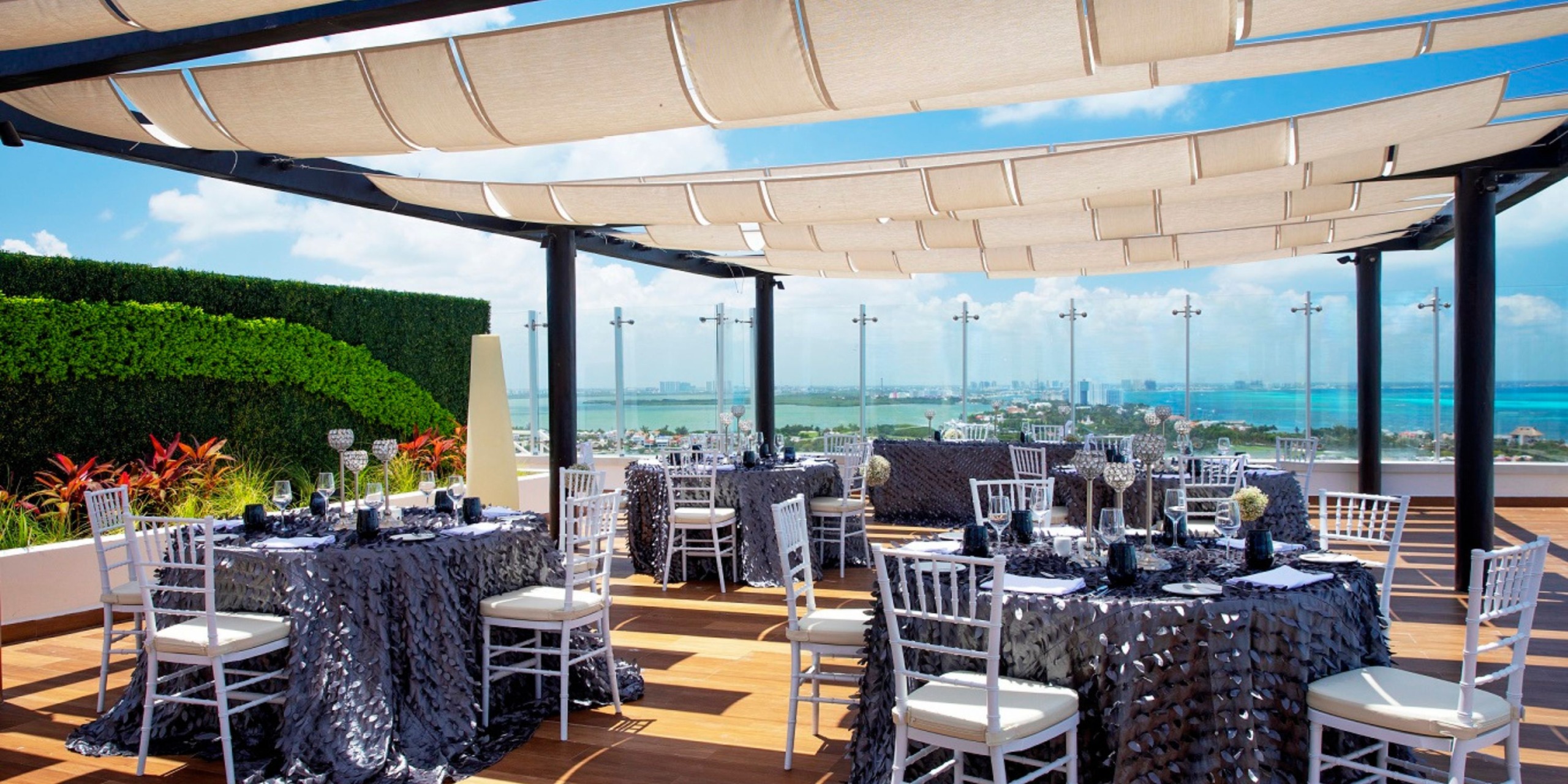 Royalton CHIC Suites Cancun presents an exquisite rooftop terrace, perfect for a destination wedding, featuring tables and white chairs that overlook stunning ocean views.