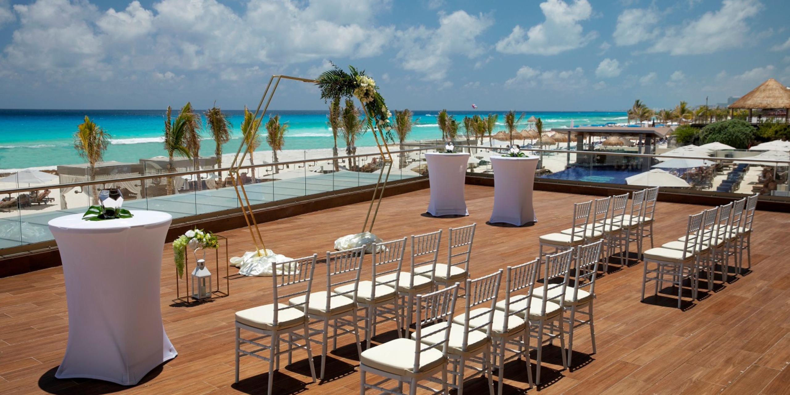 A destination wedding at Royalton CHIC Suites Cancun features a picturesque setup with chairs, tables, and a beautifully adorned arch under the clear blue sky.