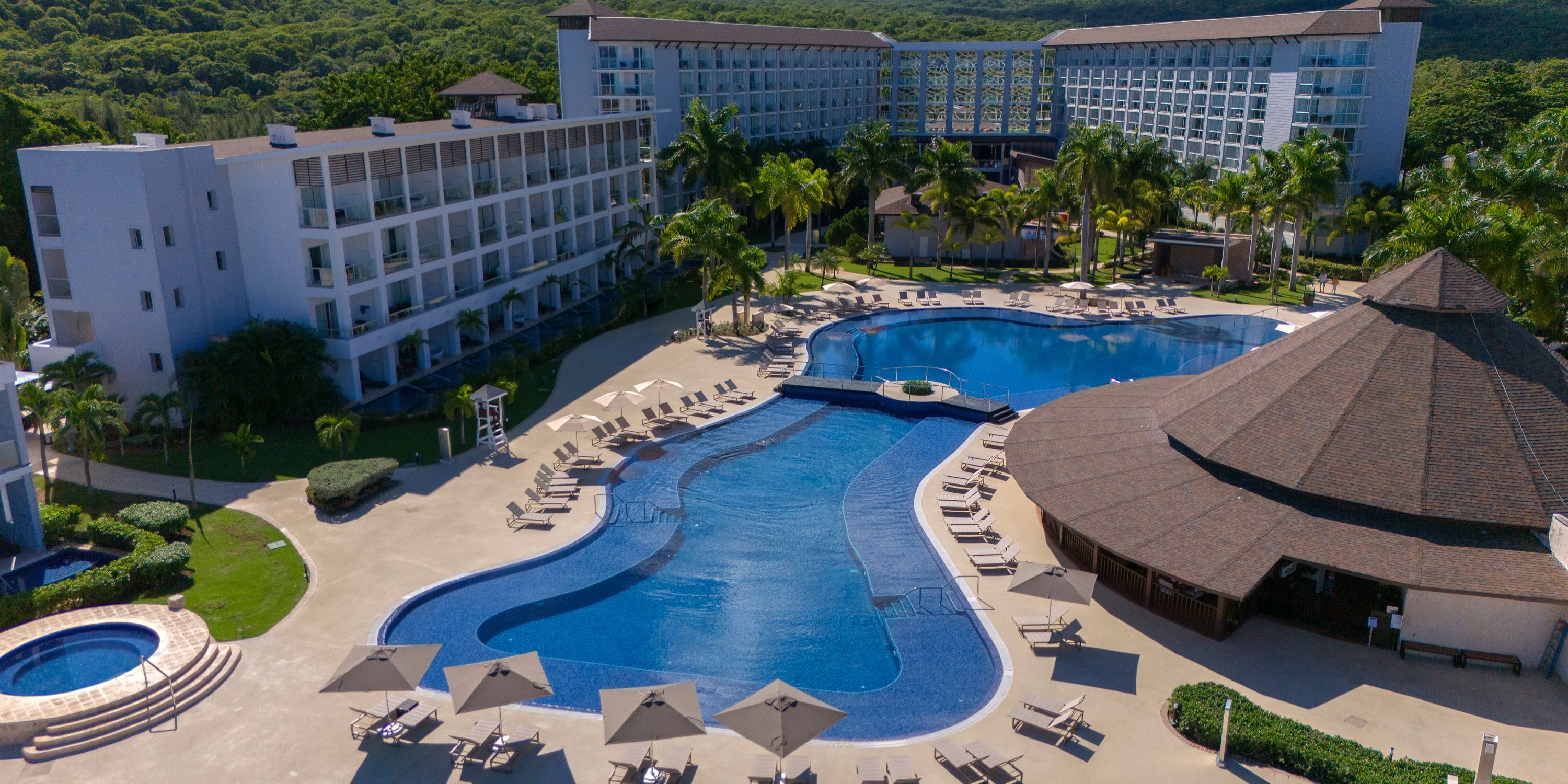 Aerial view of a large resort, perfect for a destination wedding, with pool, palm trees, and lounge chairs.