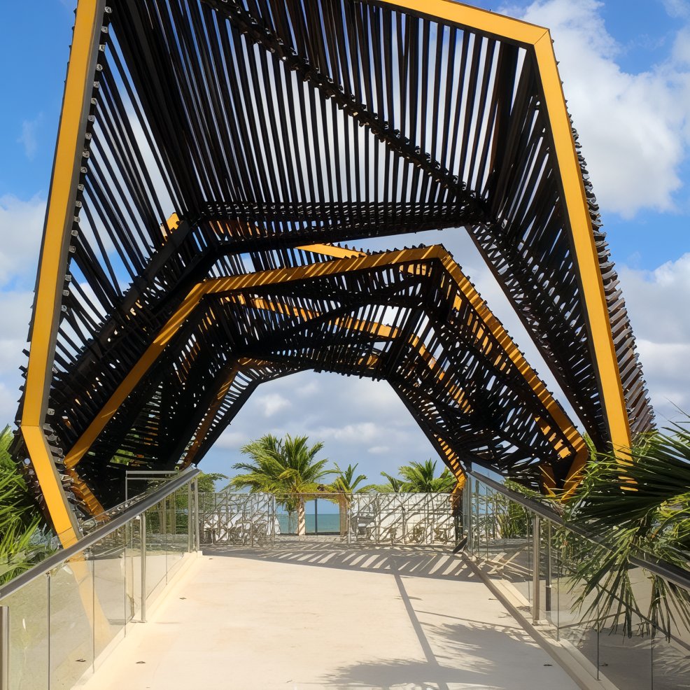 Geometric metal canopy over a walkway, perfect for a destination wedding, with palms and ocean behind.