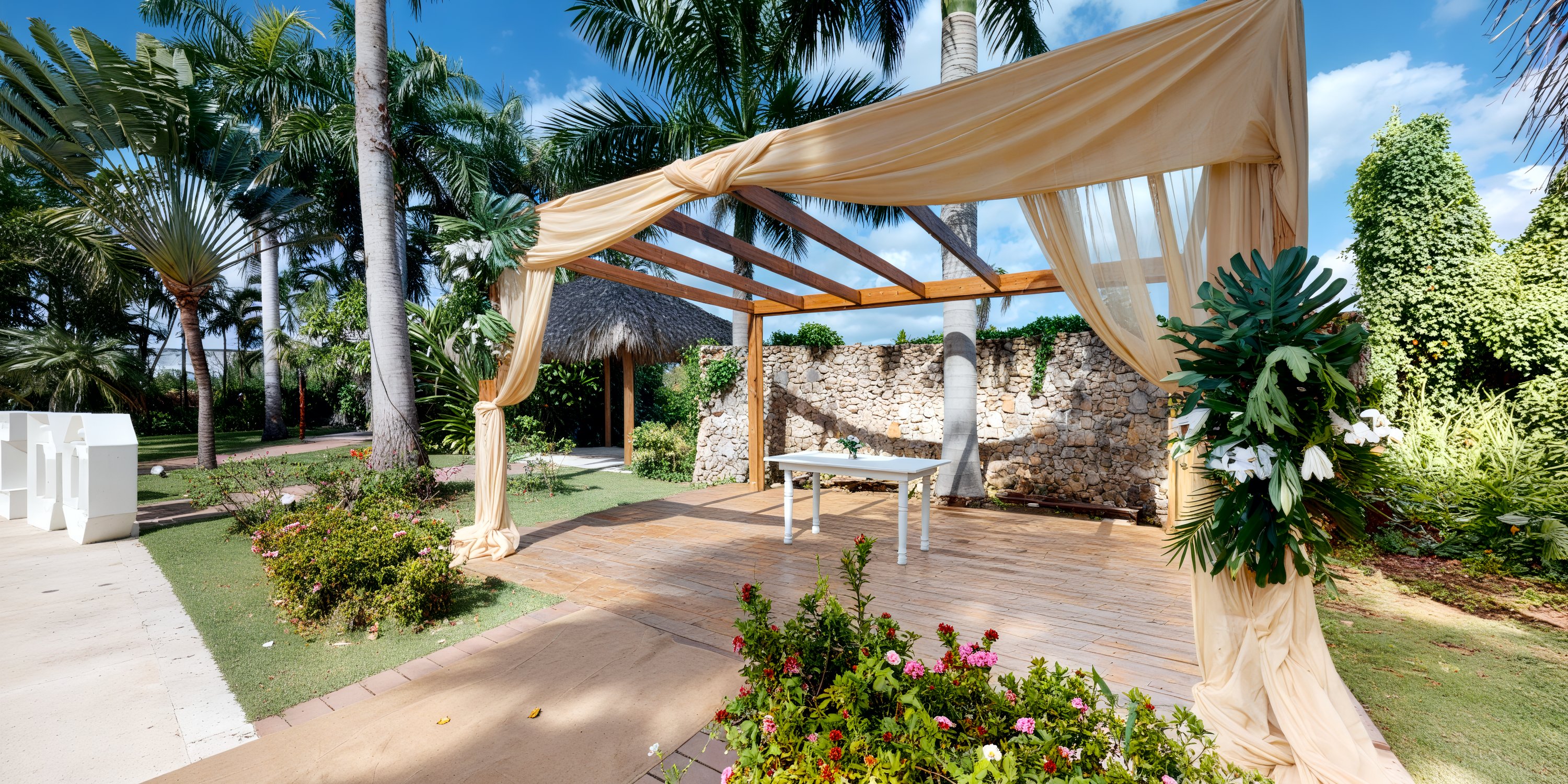 A destination wedding ceremony set on a wooden deck featuring an altar adorned with elegant fabric draping and vibrant tropical foliage.