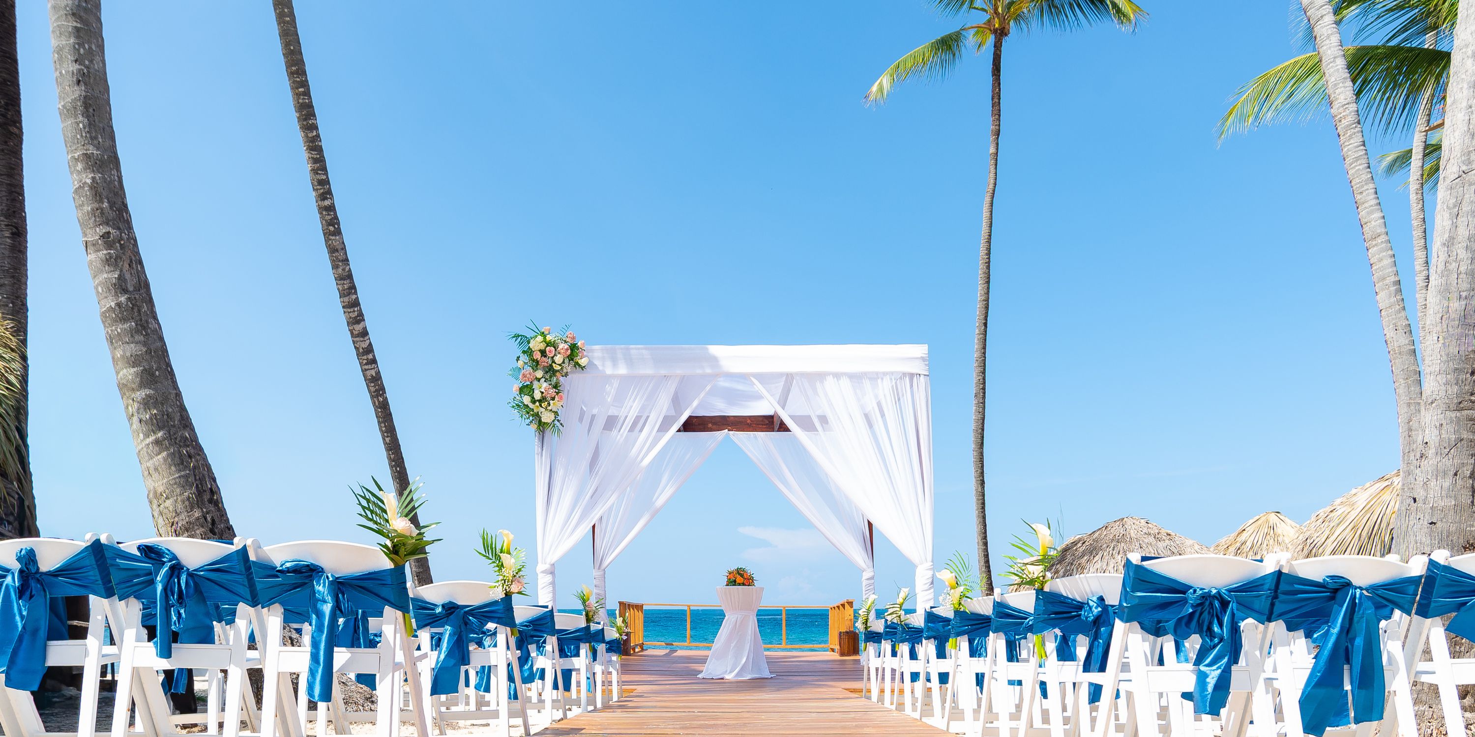 Destination wedding at Royalton Splash Punta Cana: white chairs with blue sashes, canopy by the ocean.