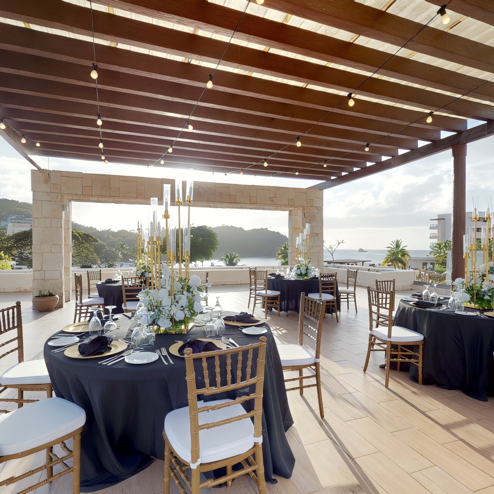 Chic destination wedding setup with round tables, black tablecloths, gold chairs, and string lights.