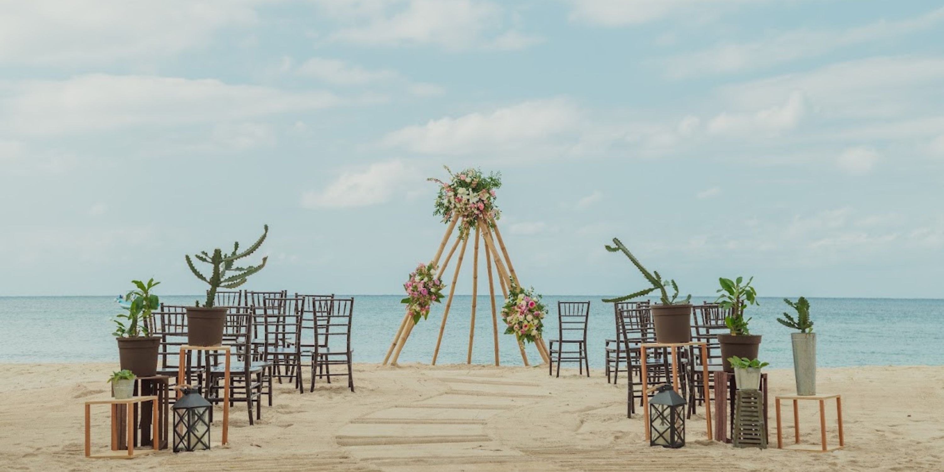 Destination wedding setup at Secrets Aura Cozumel with wooden chairs and a floral arch beneath clear skies.