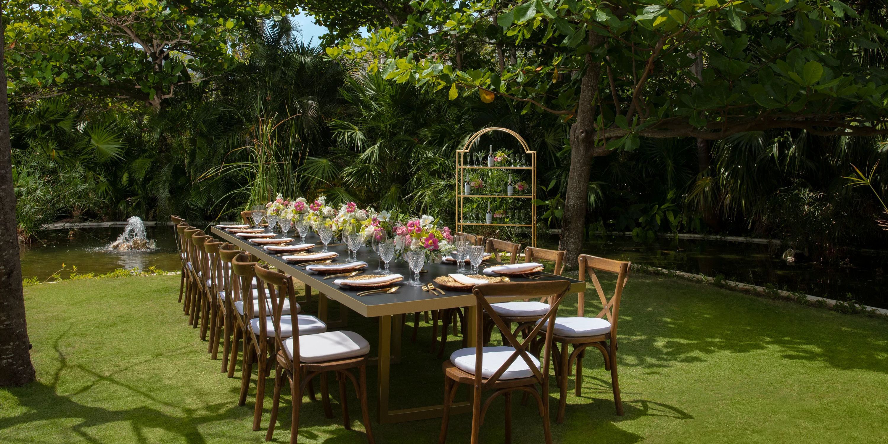 Secrets Akumal outdoor dining set for a destination wedding, adorned with flowers and plates in a lush garden.