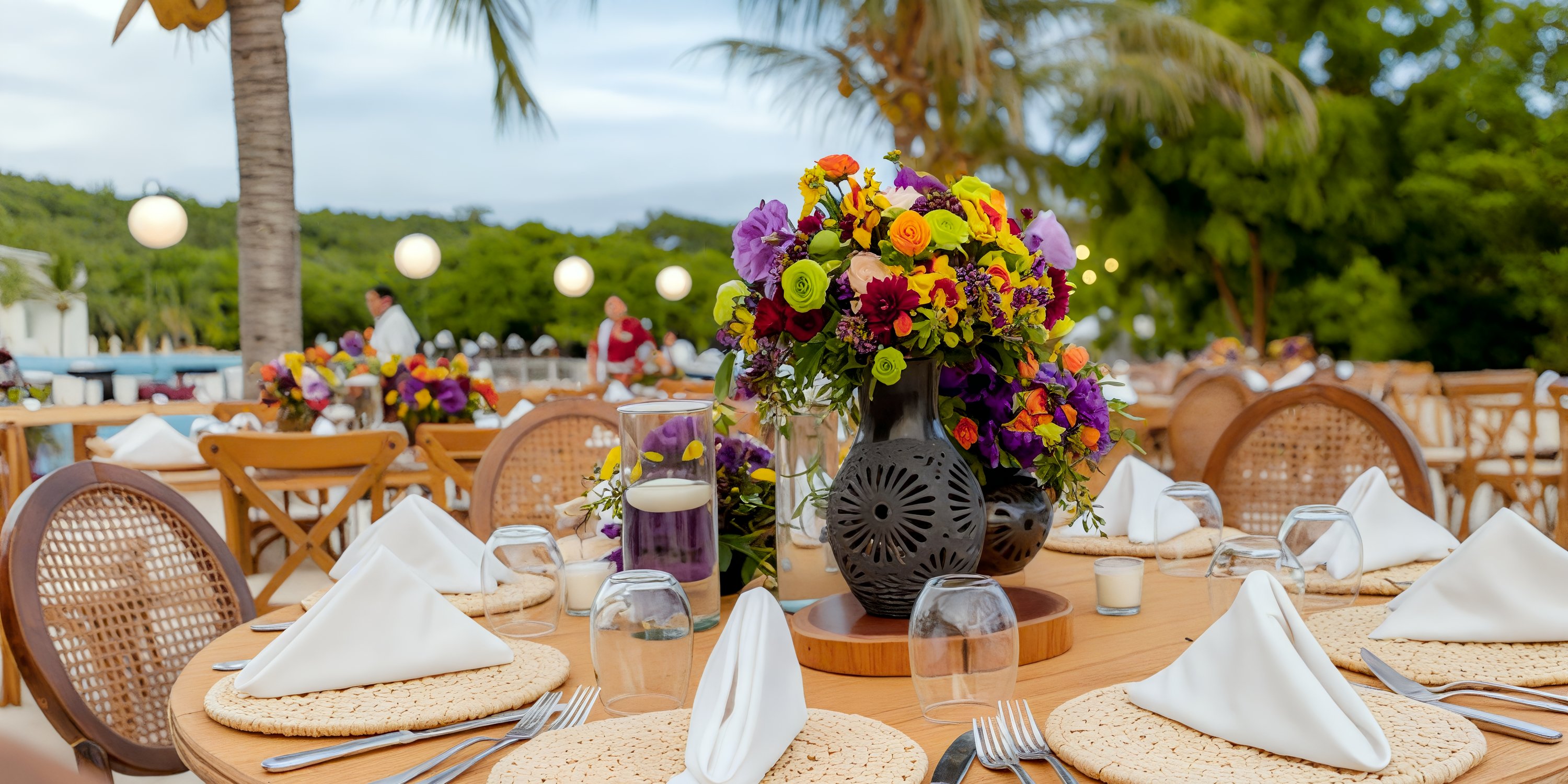 Elegant outdoor table at Secrets Huatulco set for a destination wedding, complete with plates, glasses, and a vibrant floral centerpiece.
