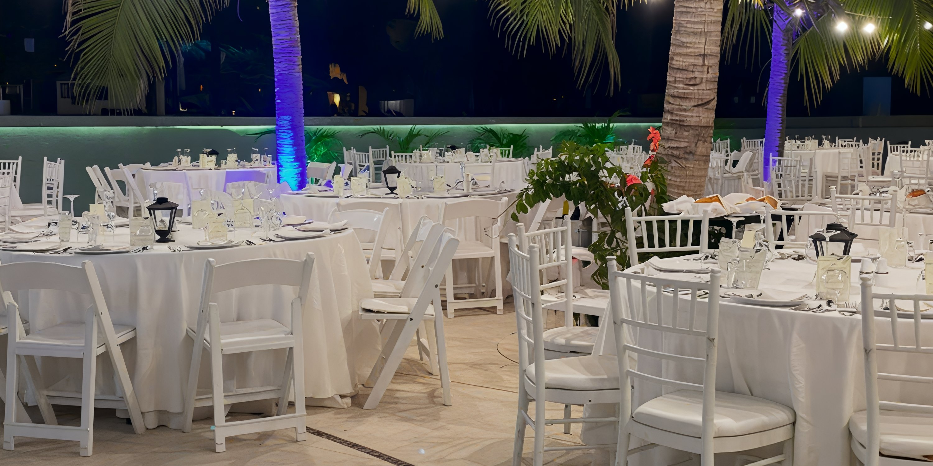 Secrets Huatulco destination wedding with round tables, white chairs, elegant tableware, and palm trees at night.