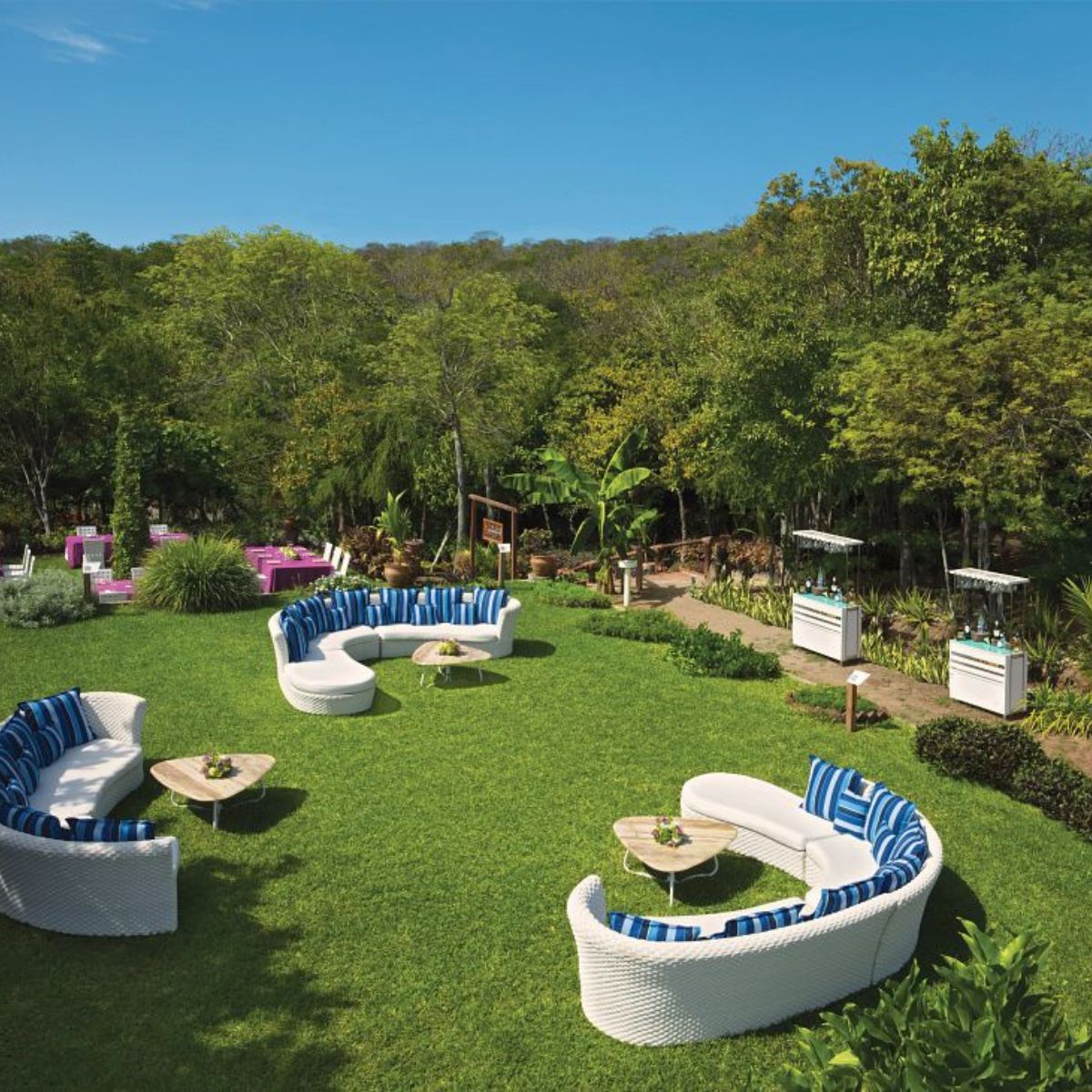 Curved white sofas on a green lawn, perfect for a destination wedding, with trees and blue sky behind.