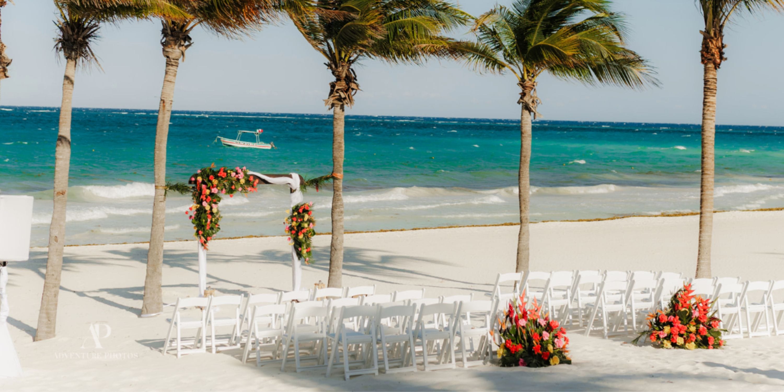 White chairs and floral arches for a destination wedding at Secrets Maroma Beach, palm trees behind.