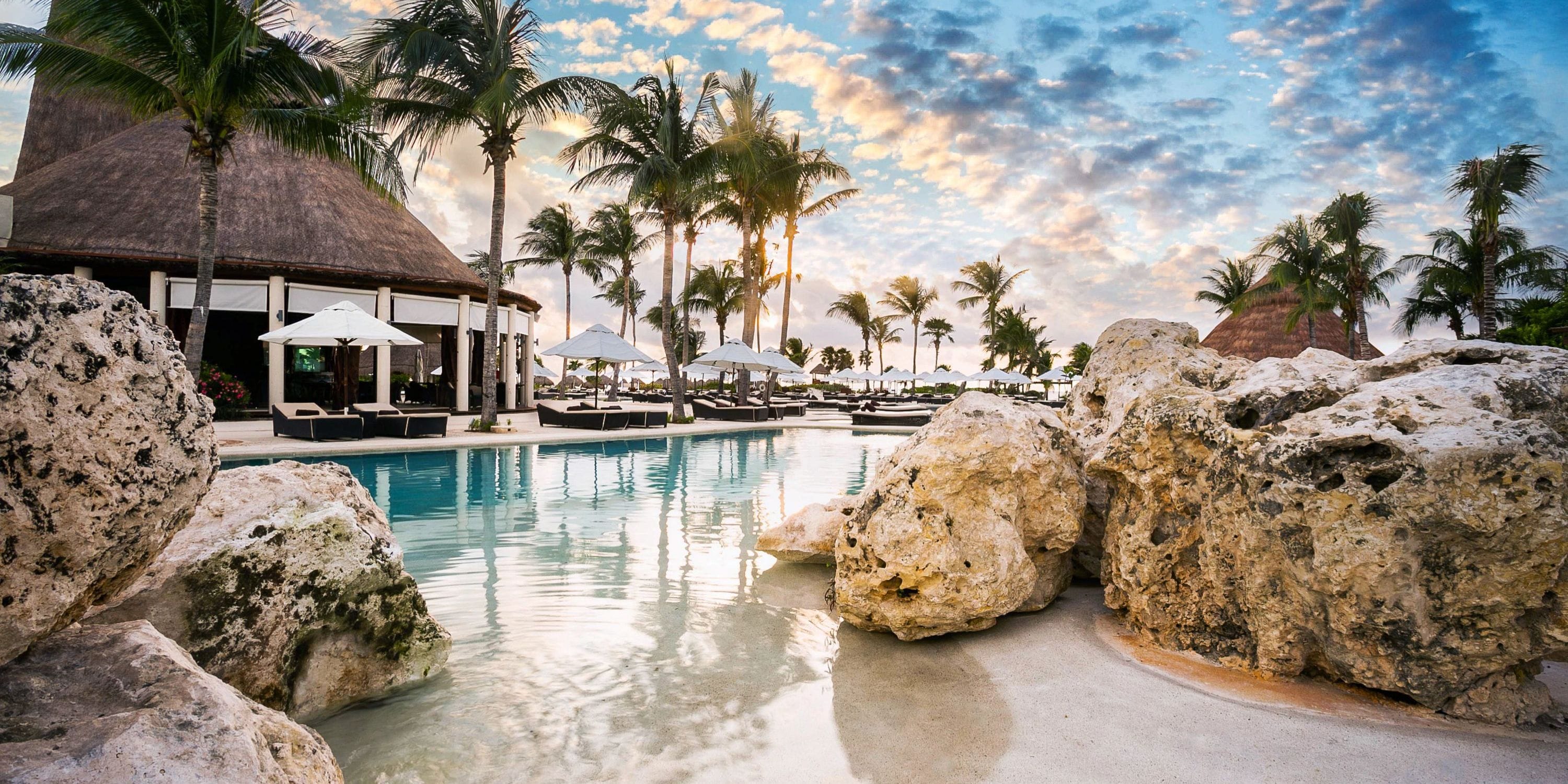 Secrets Maroma Beach pool at sunset, with palms and loungers&mdash;perfect for a destination wedding.