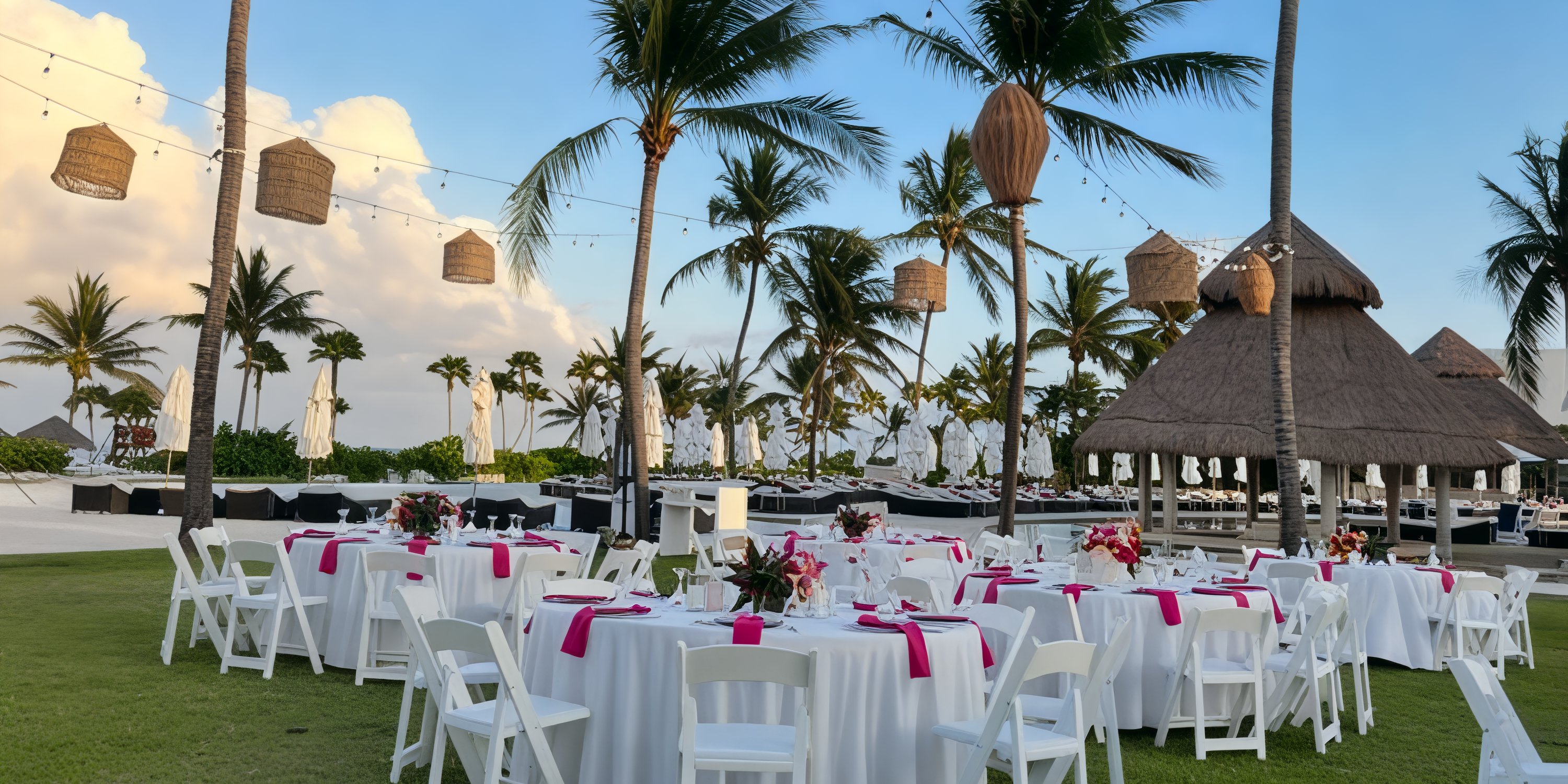 Destination wedding setup at Secrets Maroma Beach with round tables, white chairs, and pink napkins.