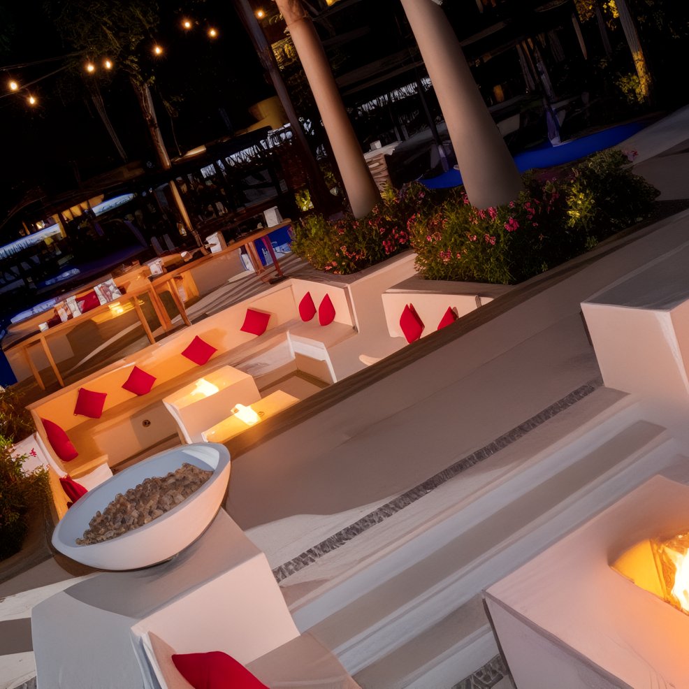 Elegant outdoor lounge area with fire pits, white seating, and red cushions, perfect for a destination wedding at night.