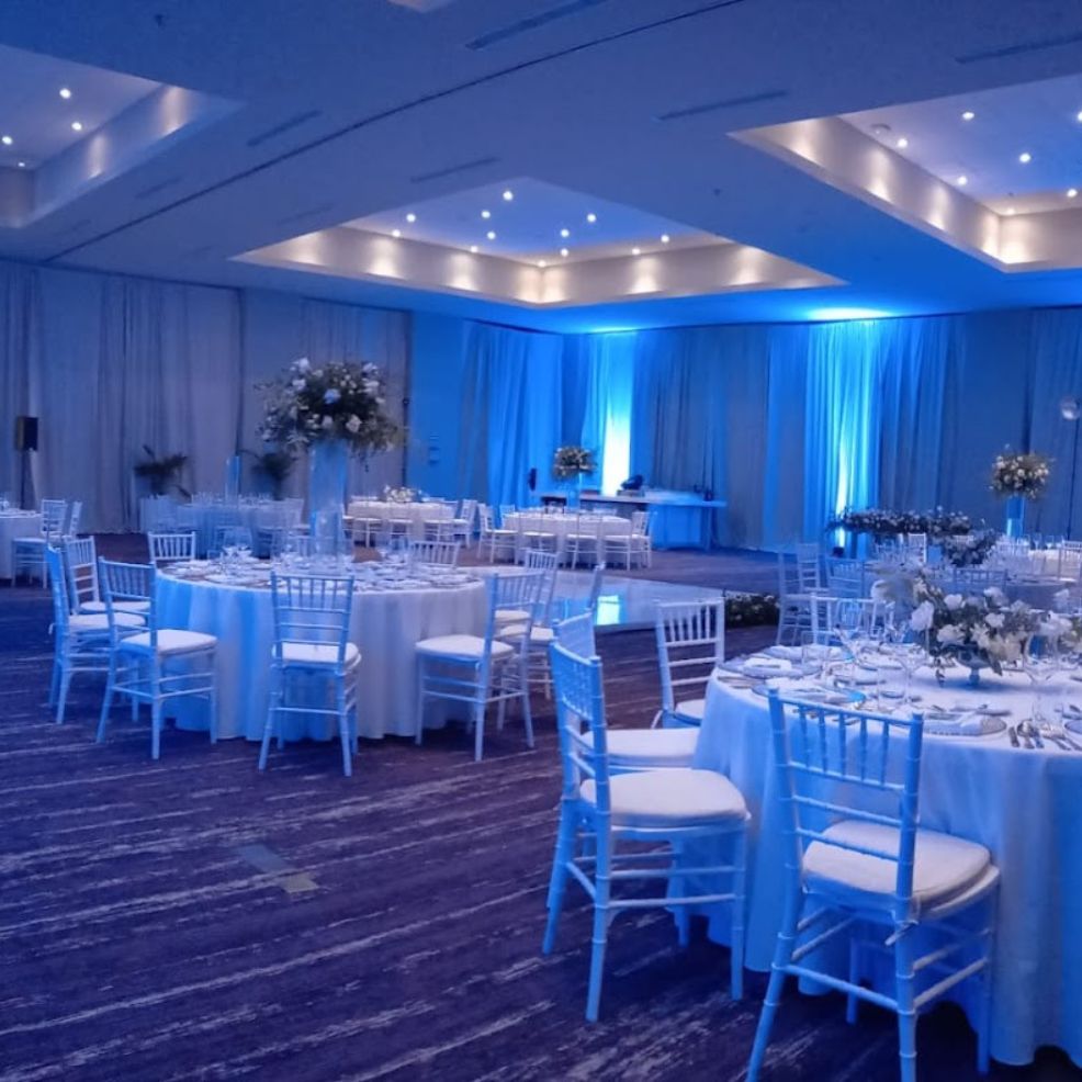 Banquet hall arranged for a destination wedding with round tables, white chairs, and blue accent lighting.