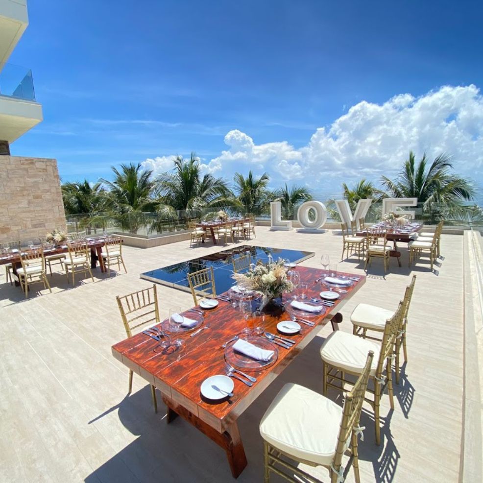 Outdoor terrace set for a destination wedding, with dining tables, pool, palm trees, and "LOVE" letters.