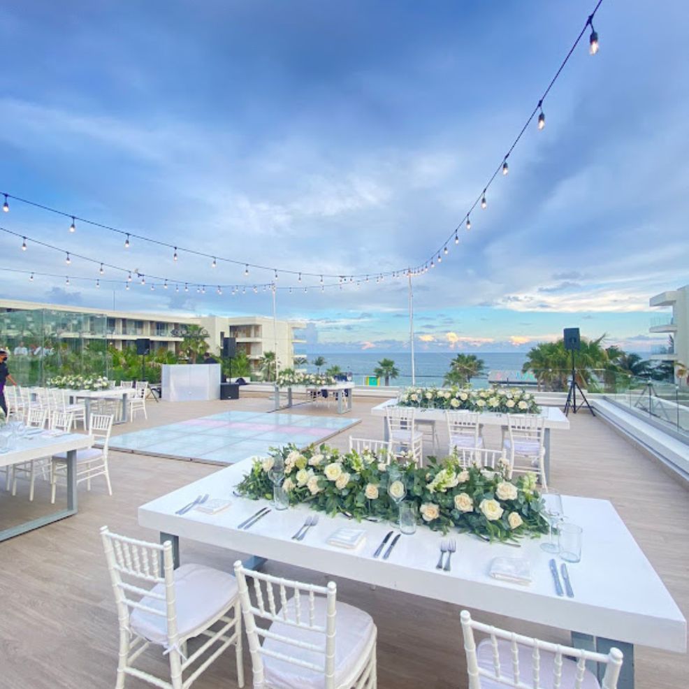 Outdoor rooftop venue set for a destination wedding, with white tables, floral centerpieces, and ocean views.