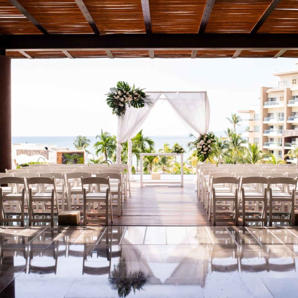 Destination wedding ceremony setup featuring white chairs and a floral arch overlooking the ocean.