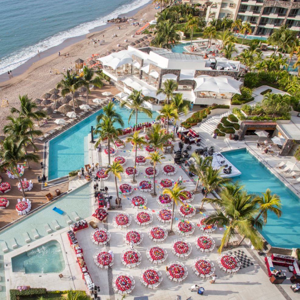 Aerial view of a beachside resort with pools and outdoor tables arranged for a destination wedding event.