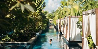 Person swims at Secrets Royal Beach, a tropical poolside popular for destination weddings, with plants and cabanas.