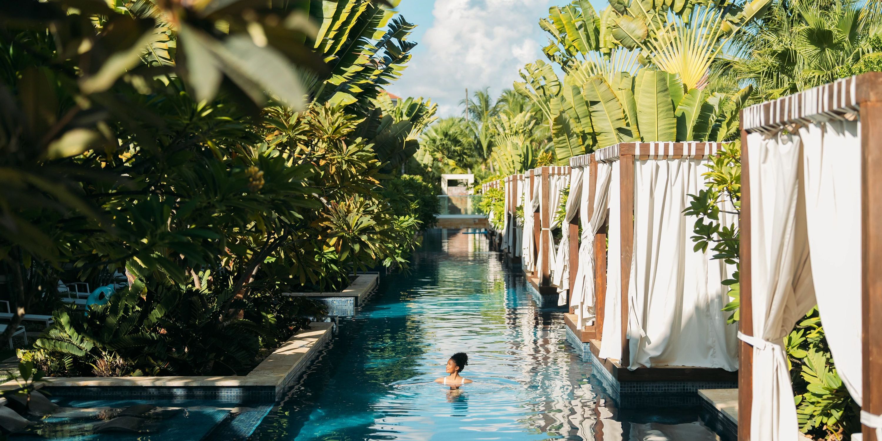 Person swims at Secrets Royal Beach, a tropical poolside popular for destination weddings, with plants and cabanas.