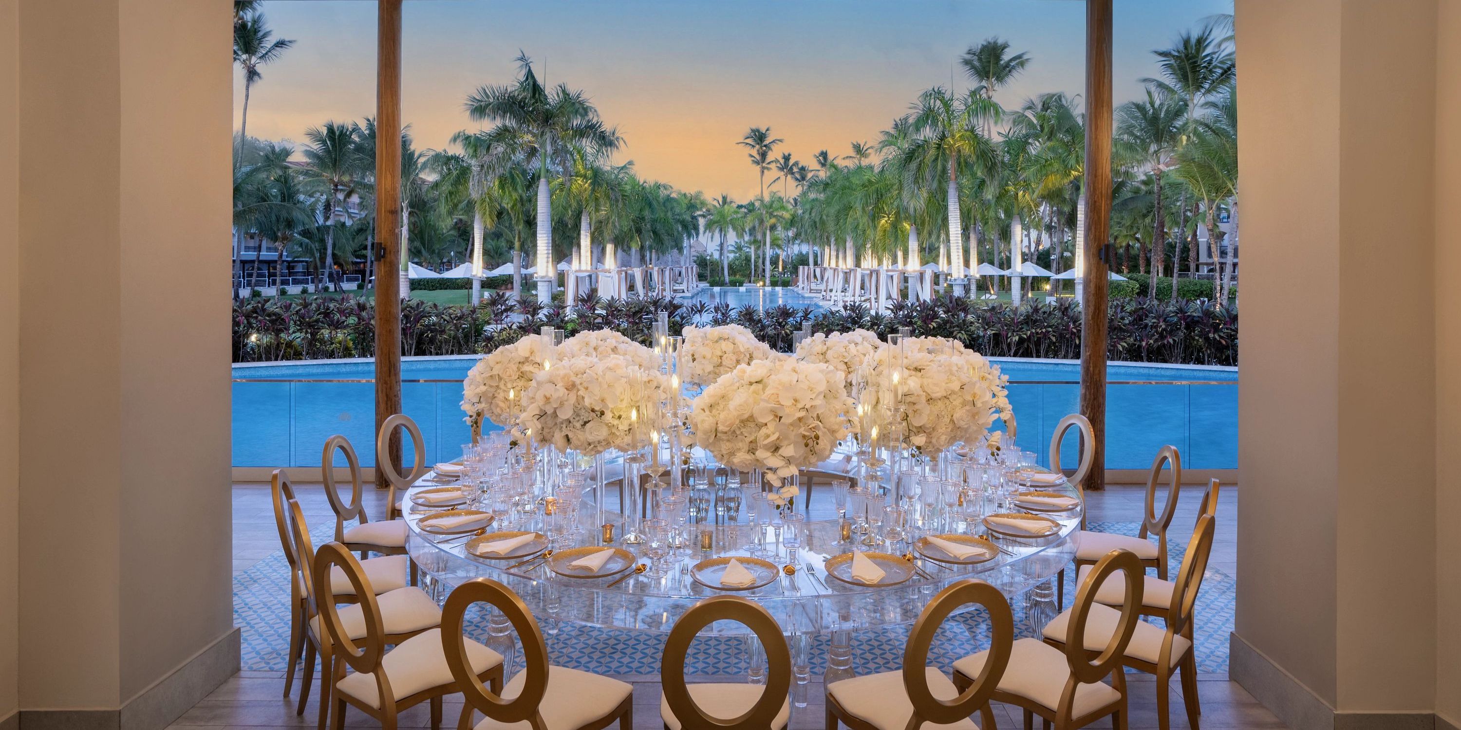 Wedding round table with white floral centerpieces by the pool at sunset, Secrets Royal Beach.