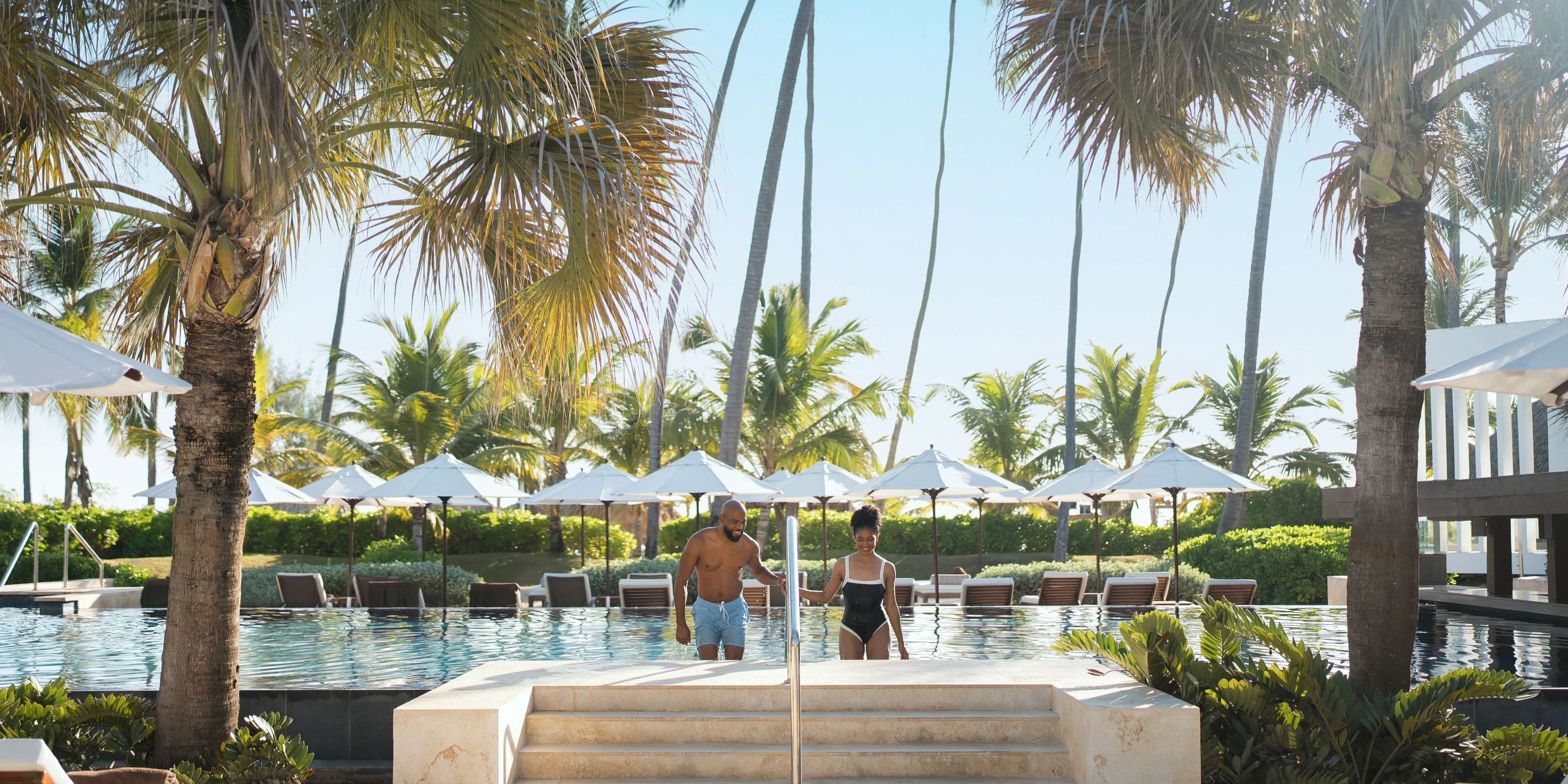 Two people walk into the pool at Secrets Royal Beach, a popular destination wedding spot with palm trees.