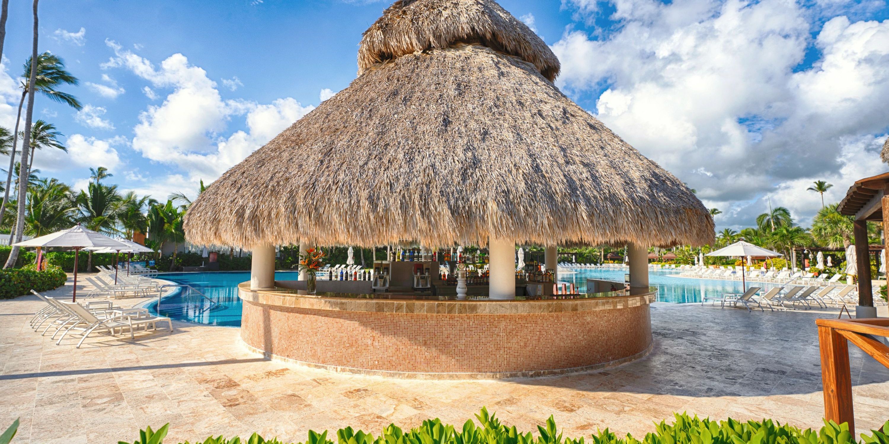 Secrets Royal Beach offers a dreamy destination wedding scene with a thatched-roof bar, chairs, and palms.