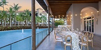 Romantic destination wedding dinner poolside at sunset, twinkling string lights at Secrets Royal Beach.