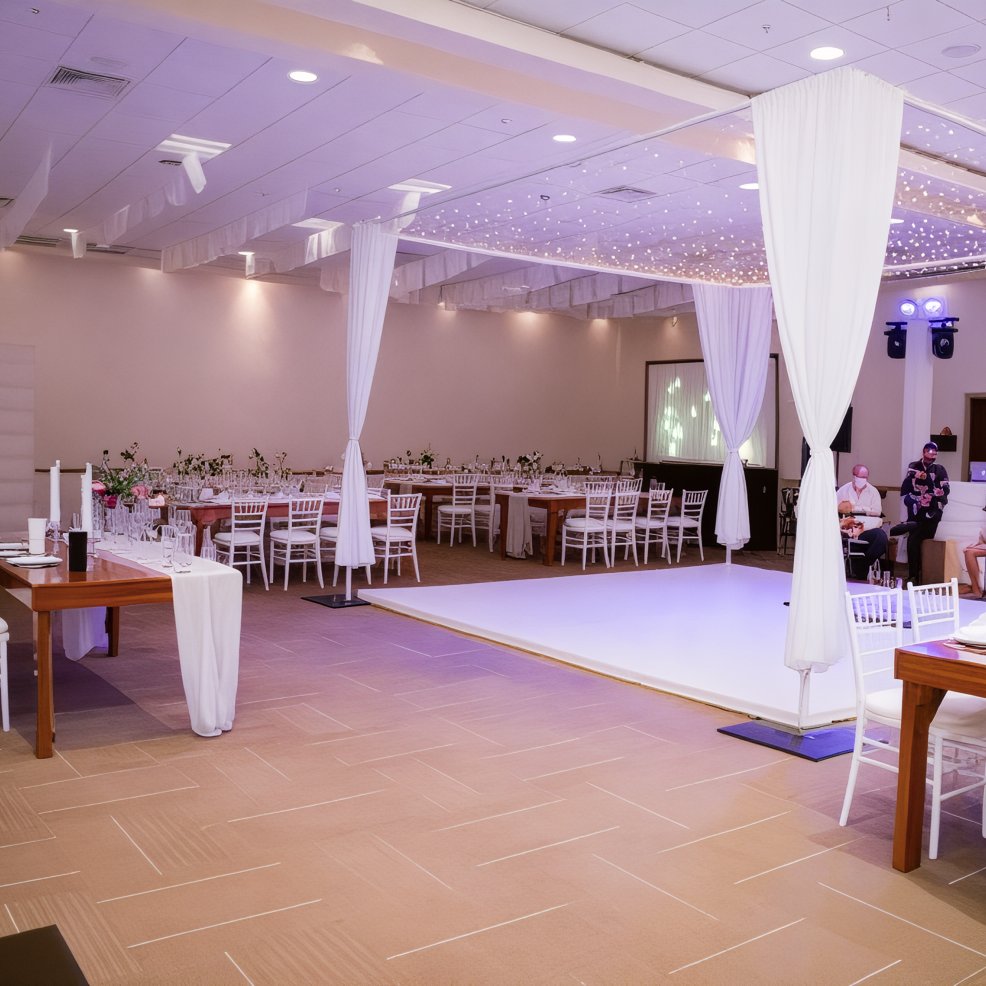 A spacious event hall adorned with elegant white decor and unoccupied tables, perfect for hosting a beautiful destination wedding.
