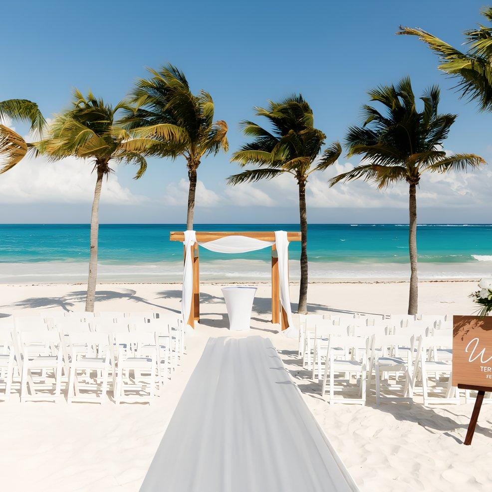 Destination wedding setup on sandy beach, palm trees, blue sea, and clear sky in the background.