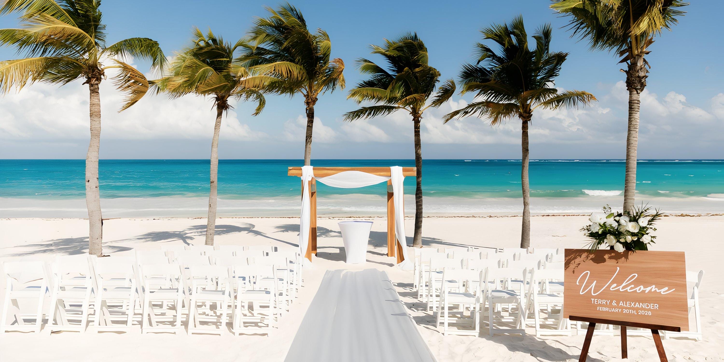 Destination wedding scene featuring white chairs, palm trees, and a decorative arch by the ocean.