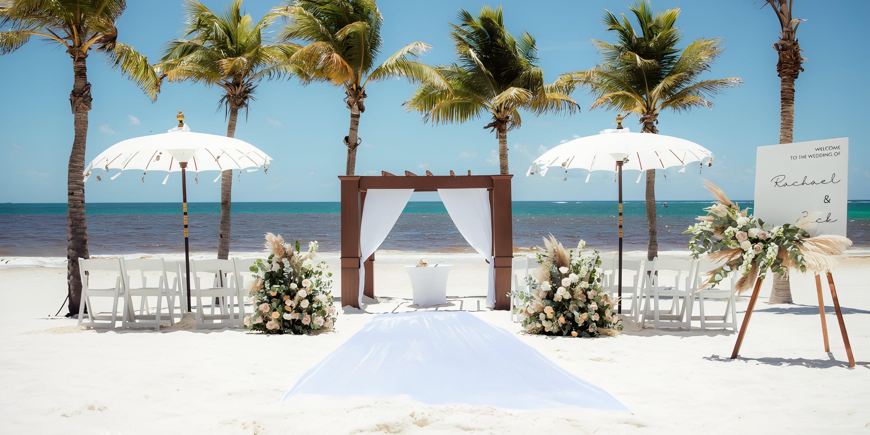Destination wedding setup on the beach with chairs, floral decor, white umbrellas, and an arch.