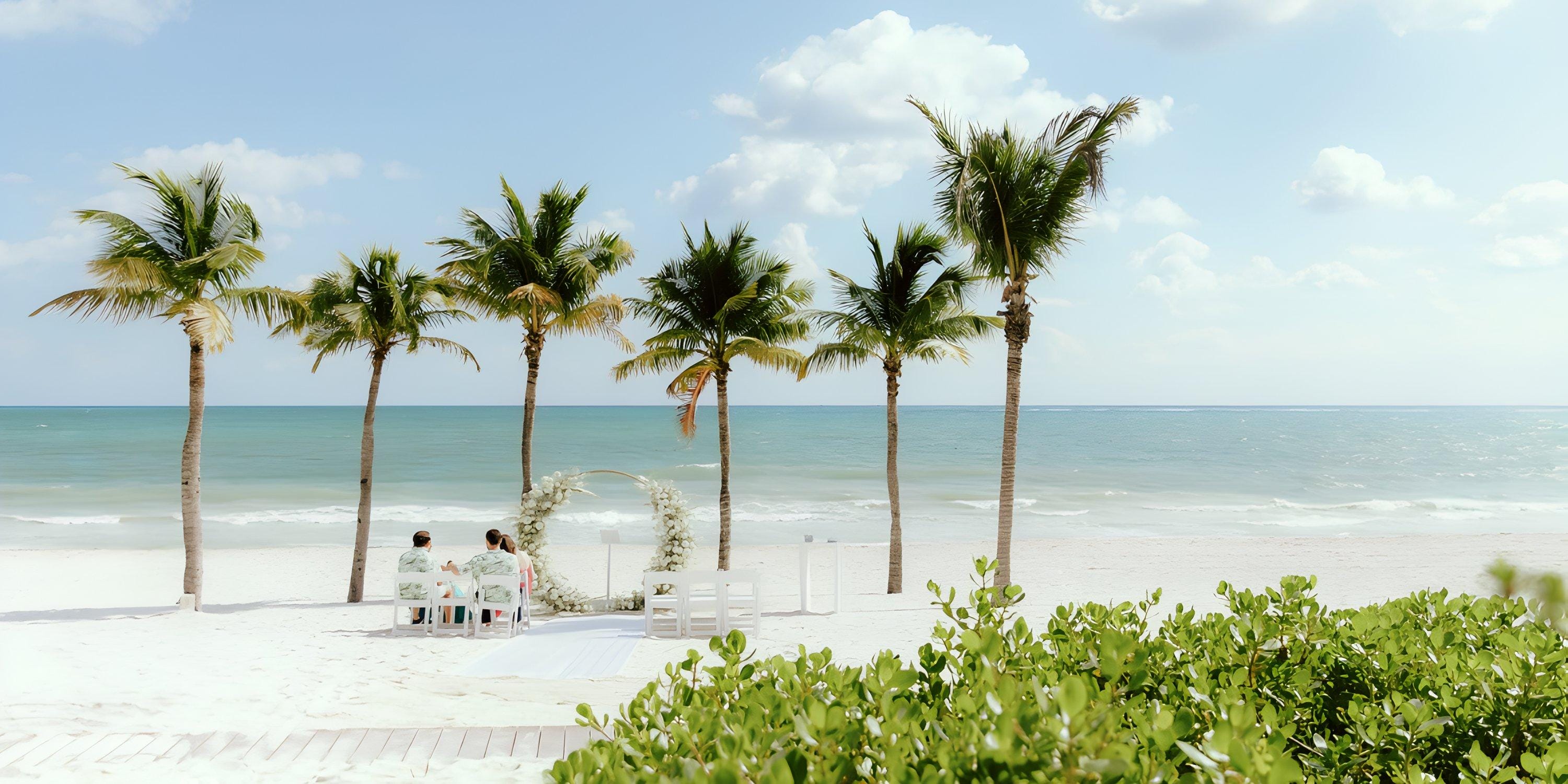A destination wedding setup on the beach, with palm trees and chairs facing the ocean.